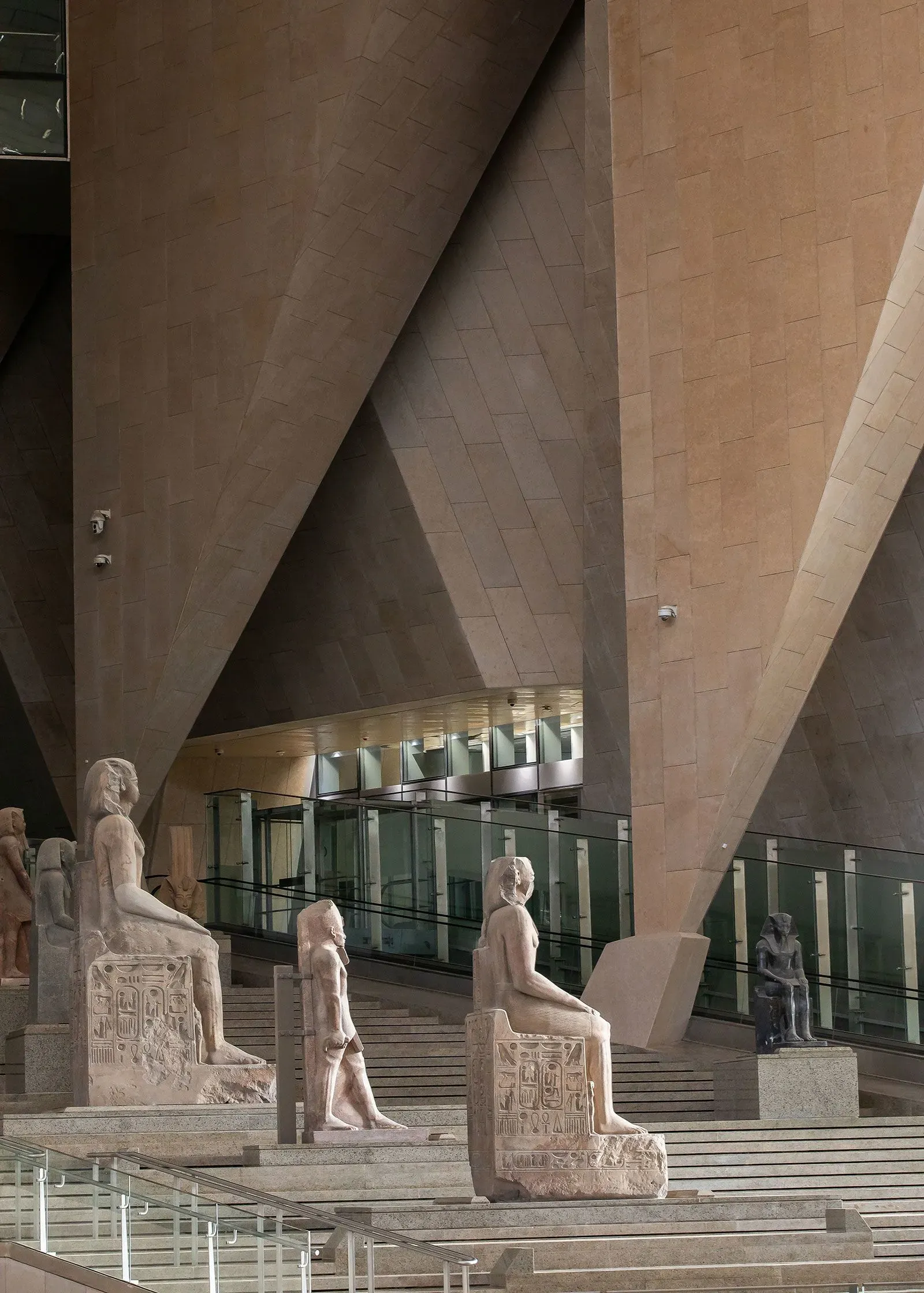 تصميم داخلي لمتحف مصري كبير، يظهر تماثيل أثرية على درجات سلم واسعة، مع جدران زجاجية وزخارف حديثة تعكس الحضارة المصرية.