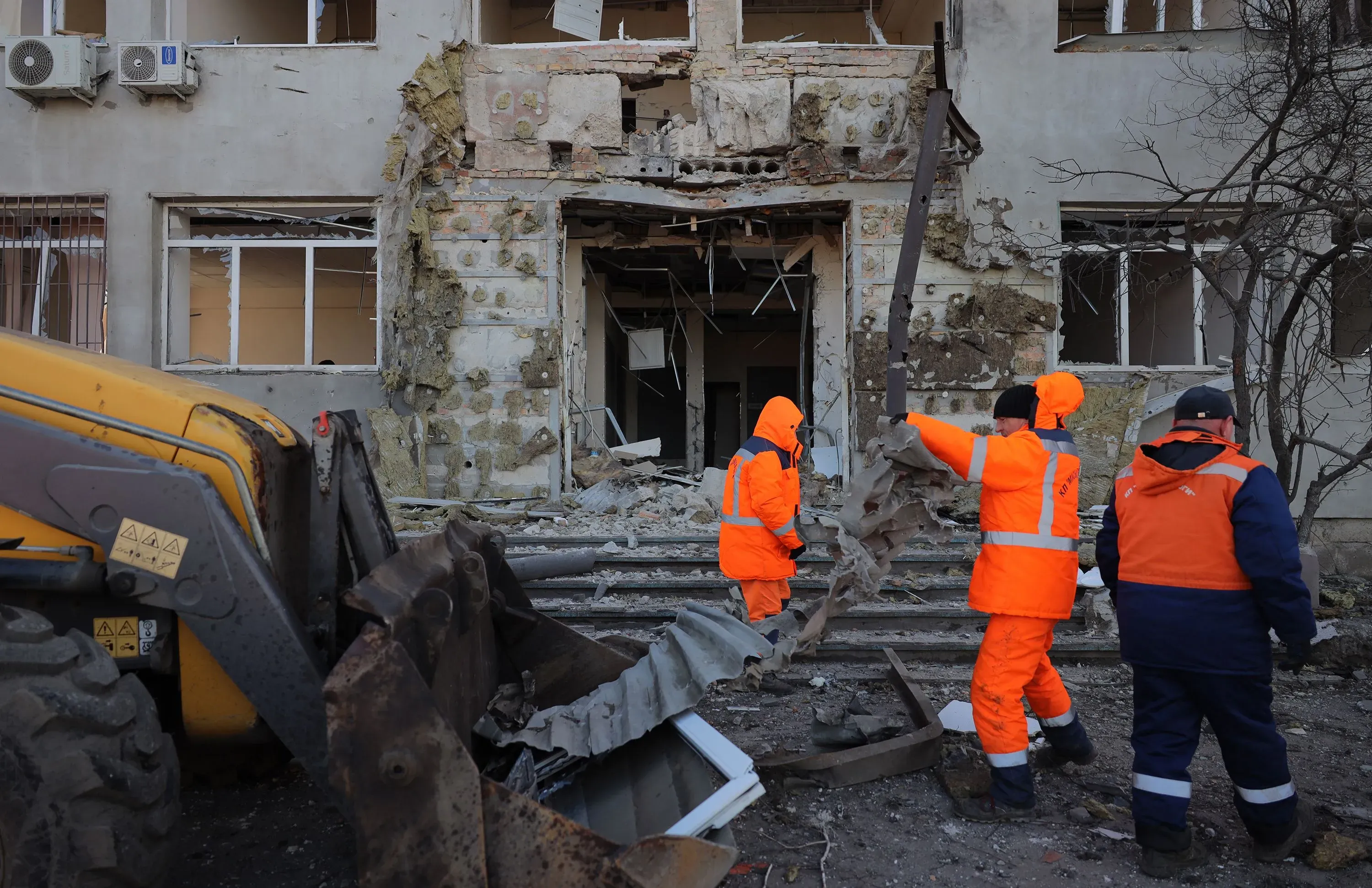 عمال إنقاذ يرتدون ملابس برتقالية يقومون بإزالة الحطام من مبنى متضرر في أوكرانيا بعد هجمات بالصواريخ والطائرات بدون طيار.