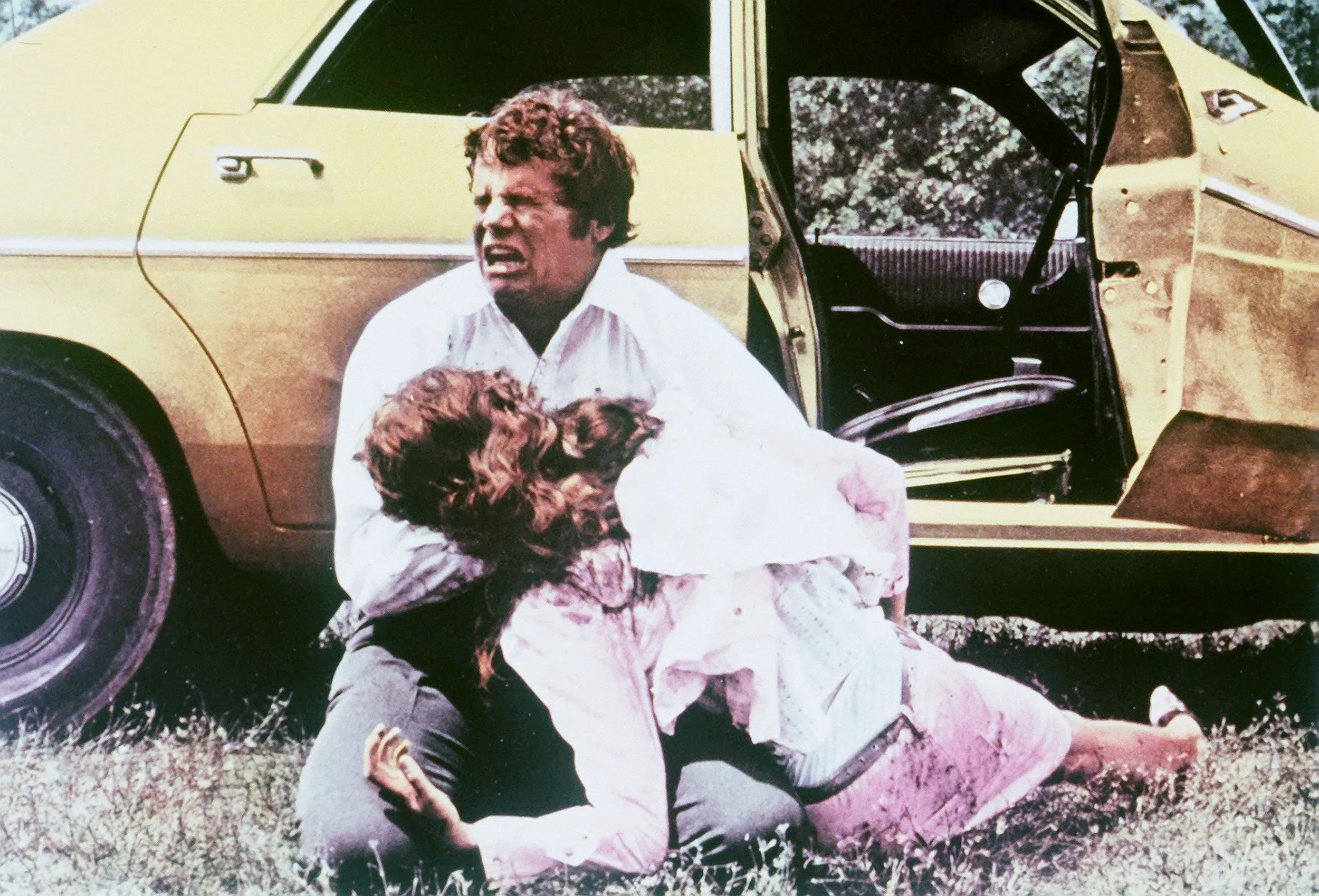 مشهد درامي من فيلم "Walking Tall" يظهر بطل الفيلم وهو يحاول إنقاذ امرأة في موقف خطير بجانب سيارة صفراء.