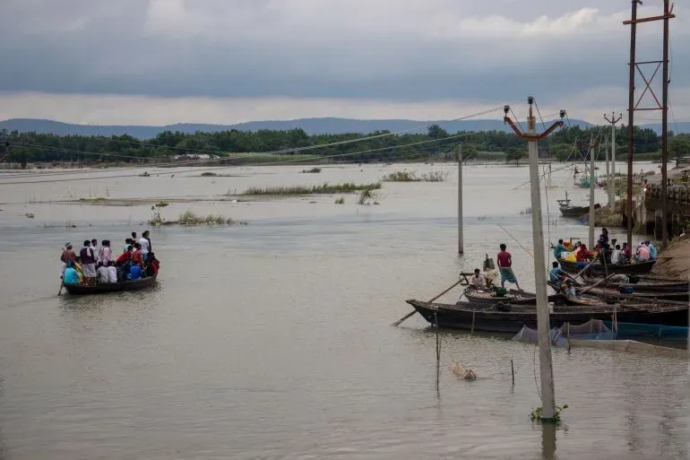 مجموعات من الأشخاص في قارب صغير يعبرون نهرًا واسعًا، مع مناظر طبيعية خضراء في الخلفية، تعكس الحياة اليومية في كيشانغانج، بيهار.