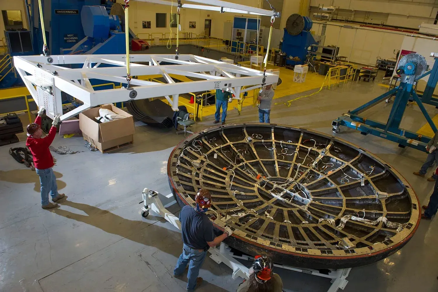 تظهر الصورة مجموعة من الفنيين أثناء تركيب الدرع الحراري لمركبة أوريون الفضائية، استعدادًا لمهمة أرتميس 2.