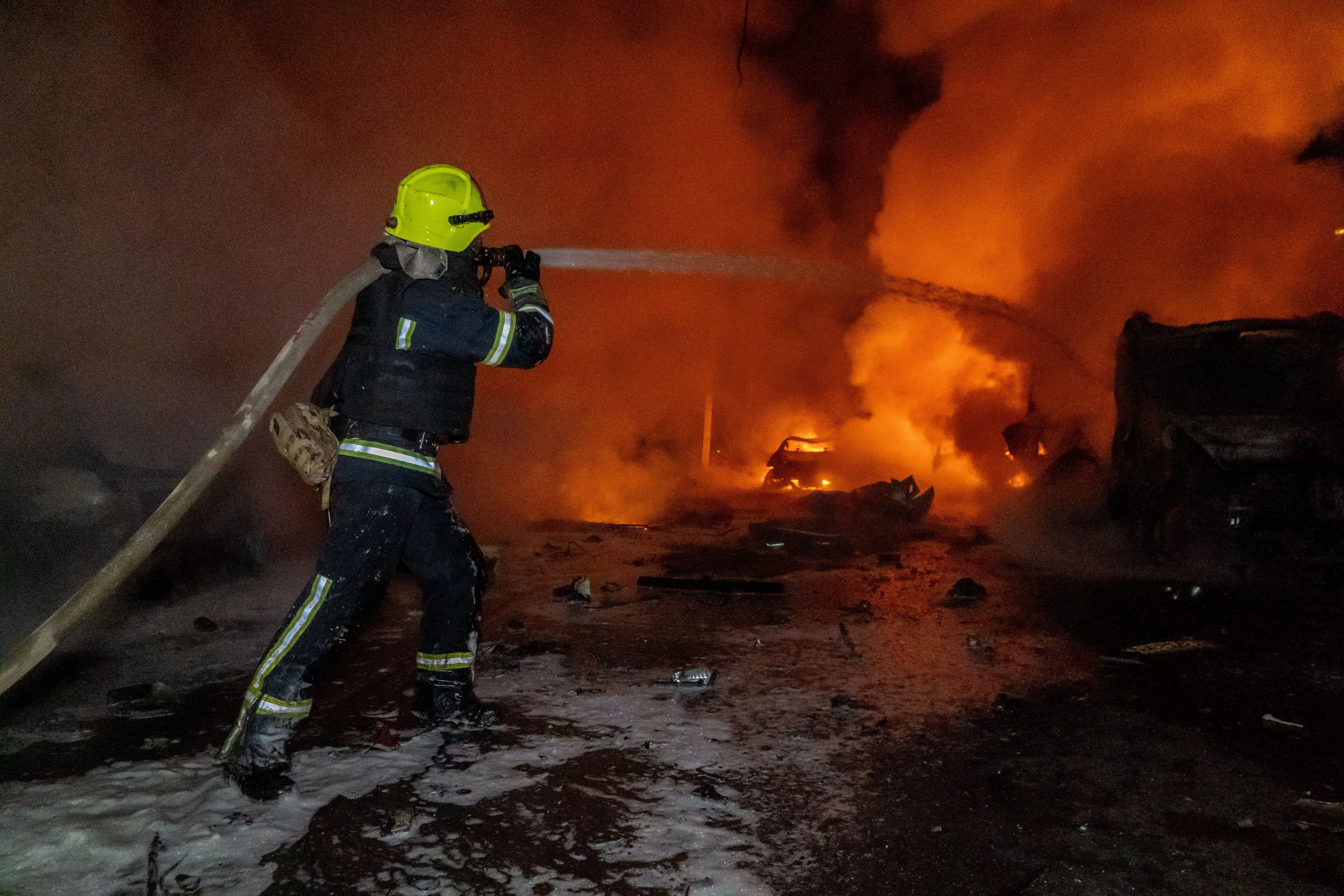 رجال الإطفاء يكافحون حريقًا هائلًا ناتجًا عن هجوم روسي في أوكرانيا، مع تصاعد الدخان والنيران في الخلفية، مما يعكس حجم الدمار.