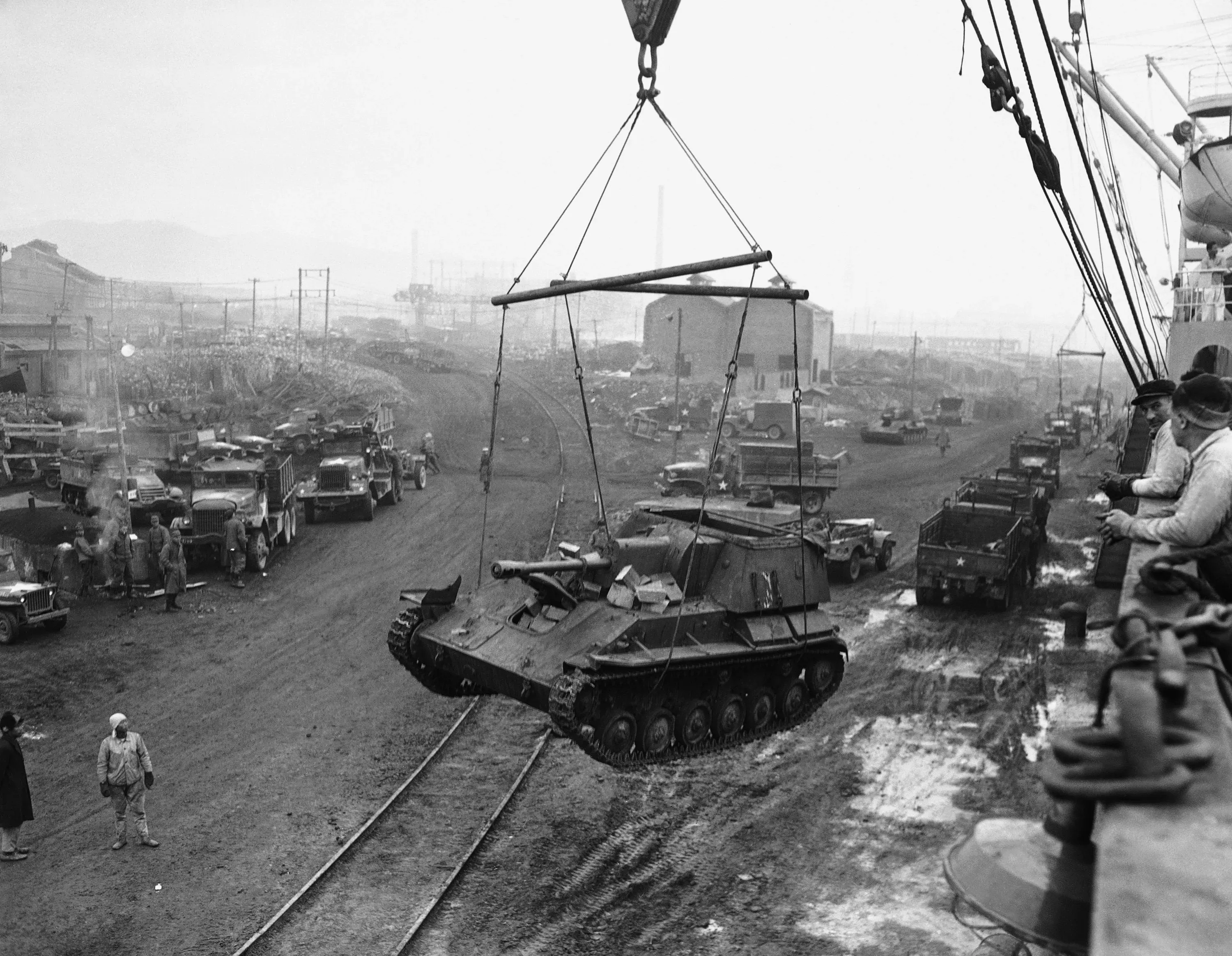 صورة تاريخية تُظهر عملية تحميل دبابة على متن سفينة شحن خلال الحرب الكورية، مع وجود جنود ومركبات في الخلفية.