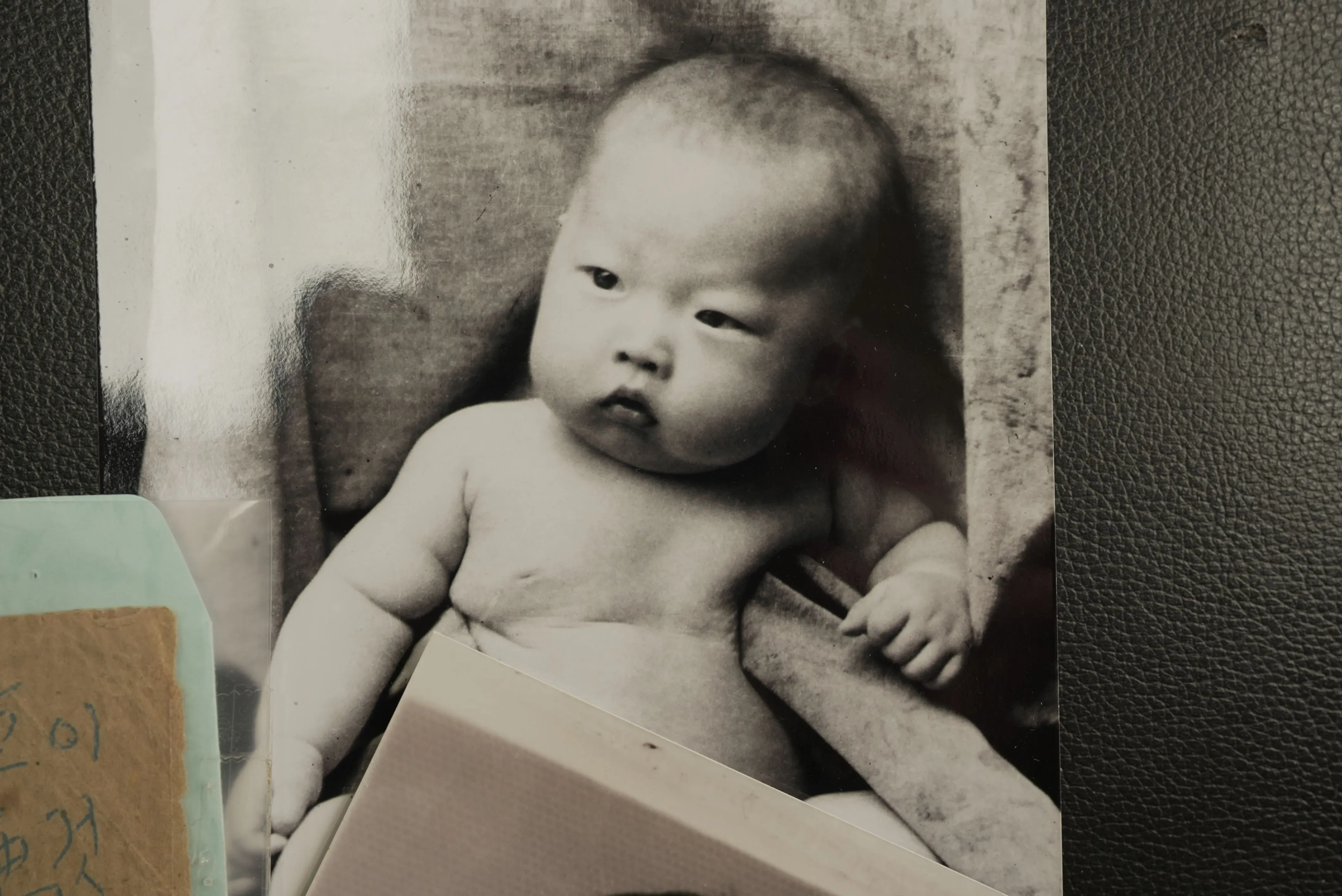 صورة لطفل حديث الولادة يُعرف باسم "كيمتشي 1"، وُلد على متن سفينة شحن أمريكية خلال الحرب الكورية، محاطًا بمستندات تعود لتلك الفترة.