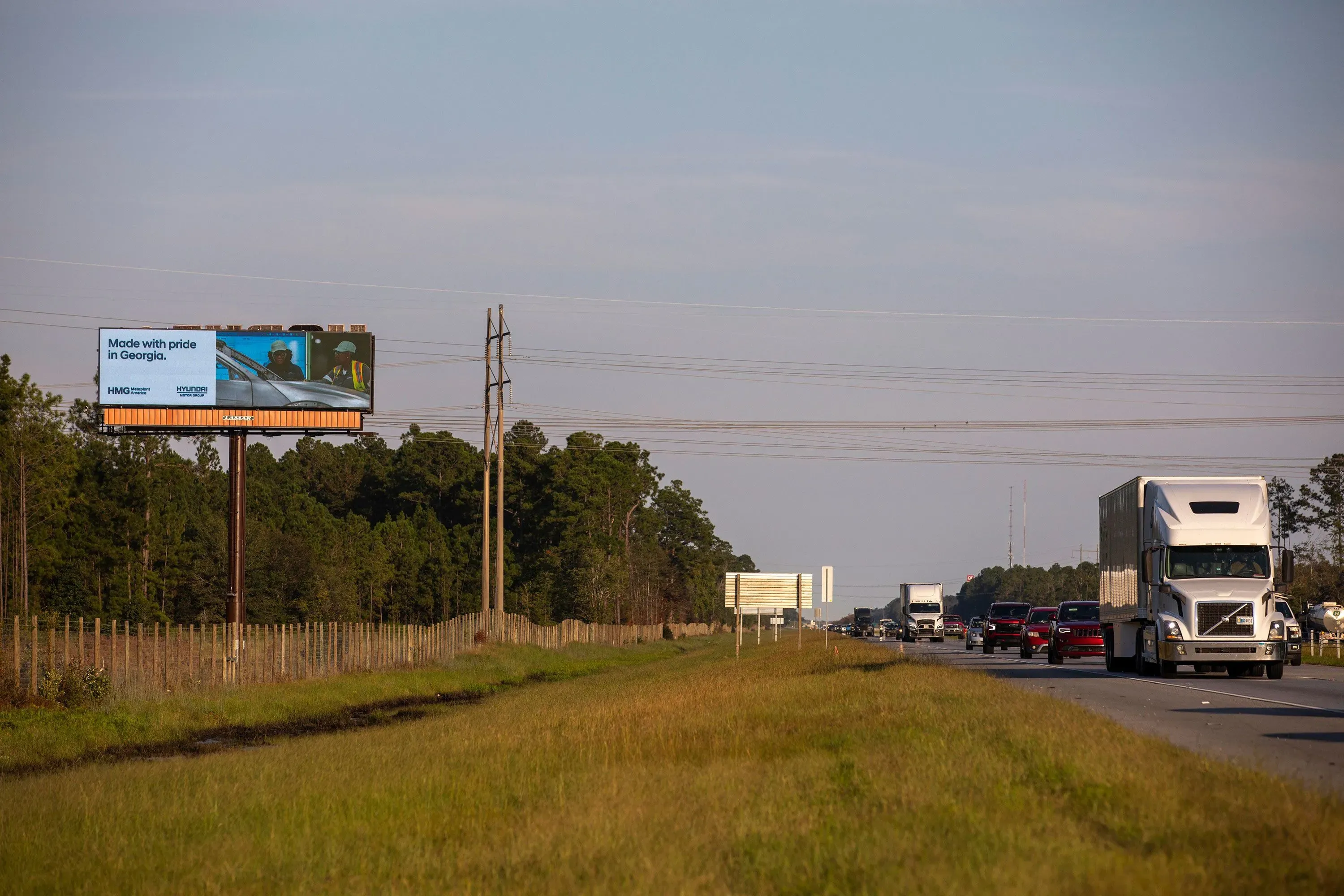 لوحة إعلانات على جانب الطريق في إيلابيل، جورجيا، تعرض عبارة "صنع بفخر في جورجيا"، مع شاحنات تسير على الطريق المحاذي.
