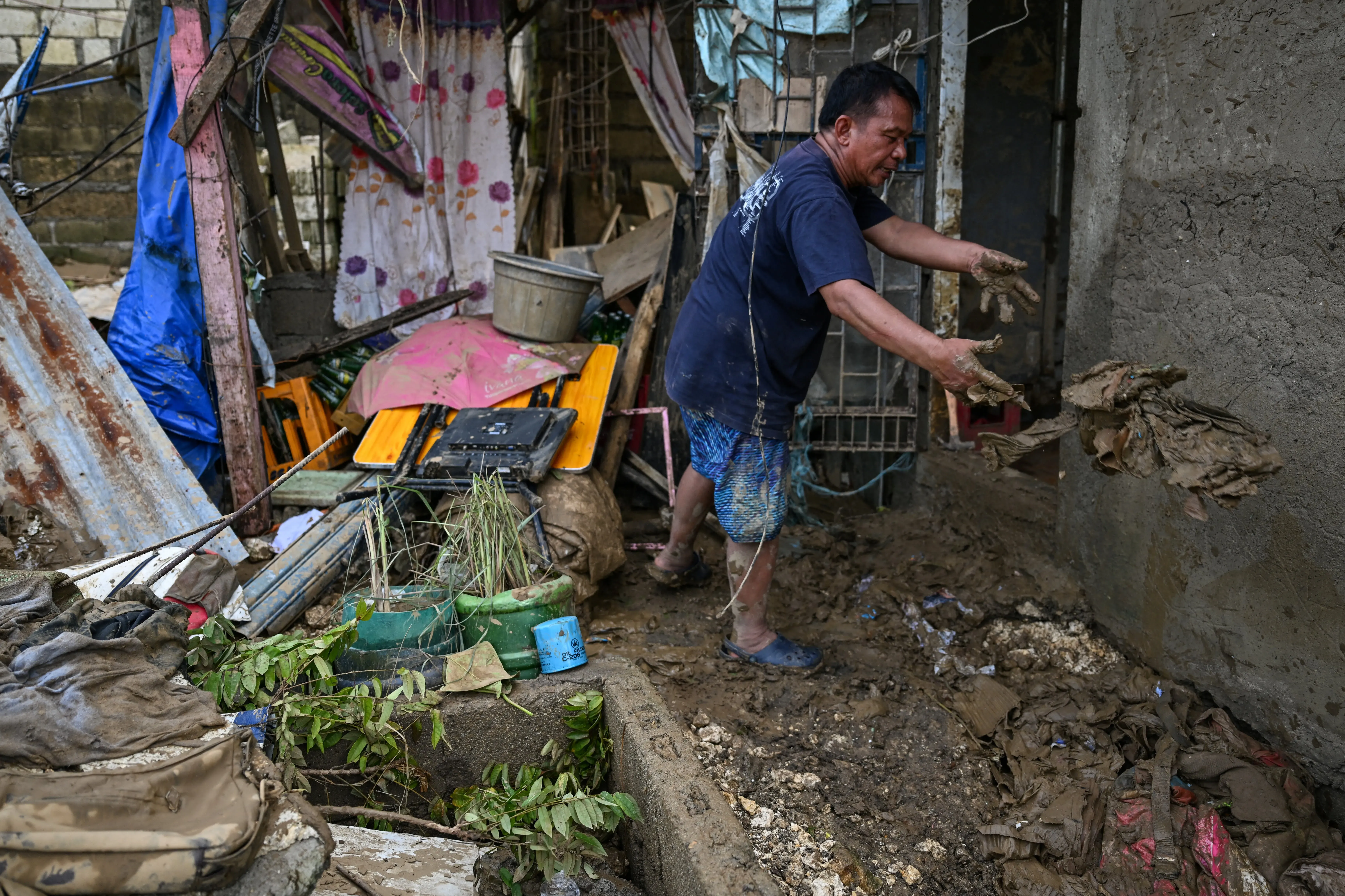 رجل ينظف الأضرار الناتجة عن إعصار كالمايجي، محاطًا بالأنقاض والوحل في منطقة سكنية متضررة في الفلبين.