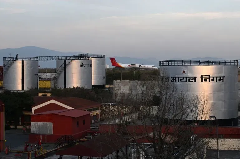 خزانات وقود في نيبال مع طائرة تقترب من الهبوط، تعكس أزمة الطاقة وتأثيرها على الاقتصاد المحلي.