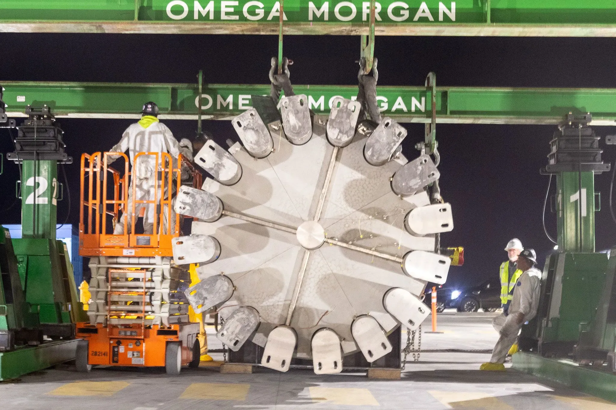 آلة حفر ضخمة تُرفع بواسطة رافعة، مع عمال يرتدون زي العمل في موقع بناء، تشير إلى جهود إعادة تشغيل محطة باليسيدس النووية.