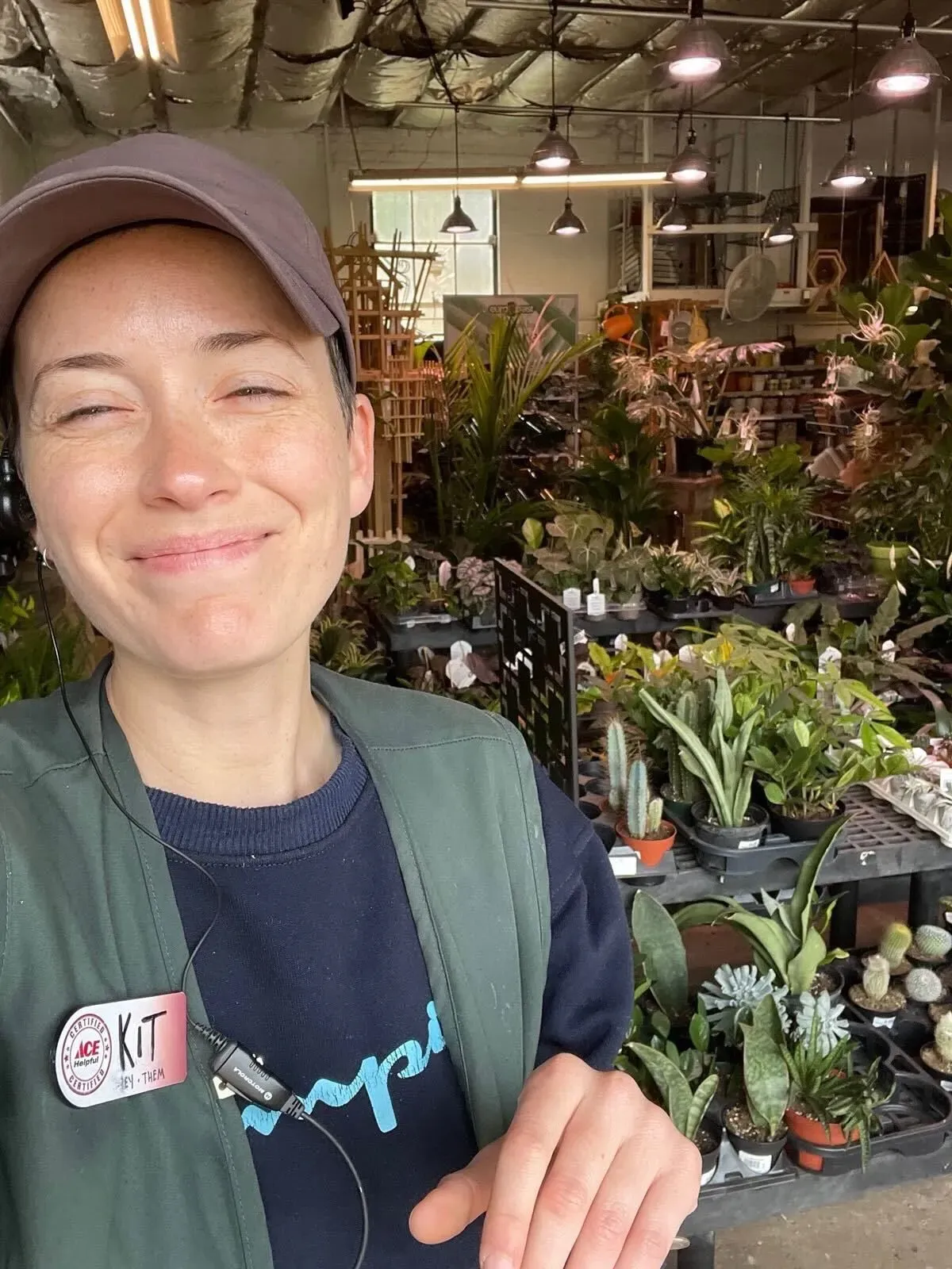 آشلي غارلي تبتسم في متجر نباتات، محاطة بالنباتات الخضراء، تعكس تحولها من العمل في الوكالة الأمريكية للتنمية الدولية إلى وظيفة جديدة.