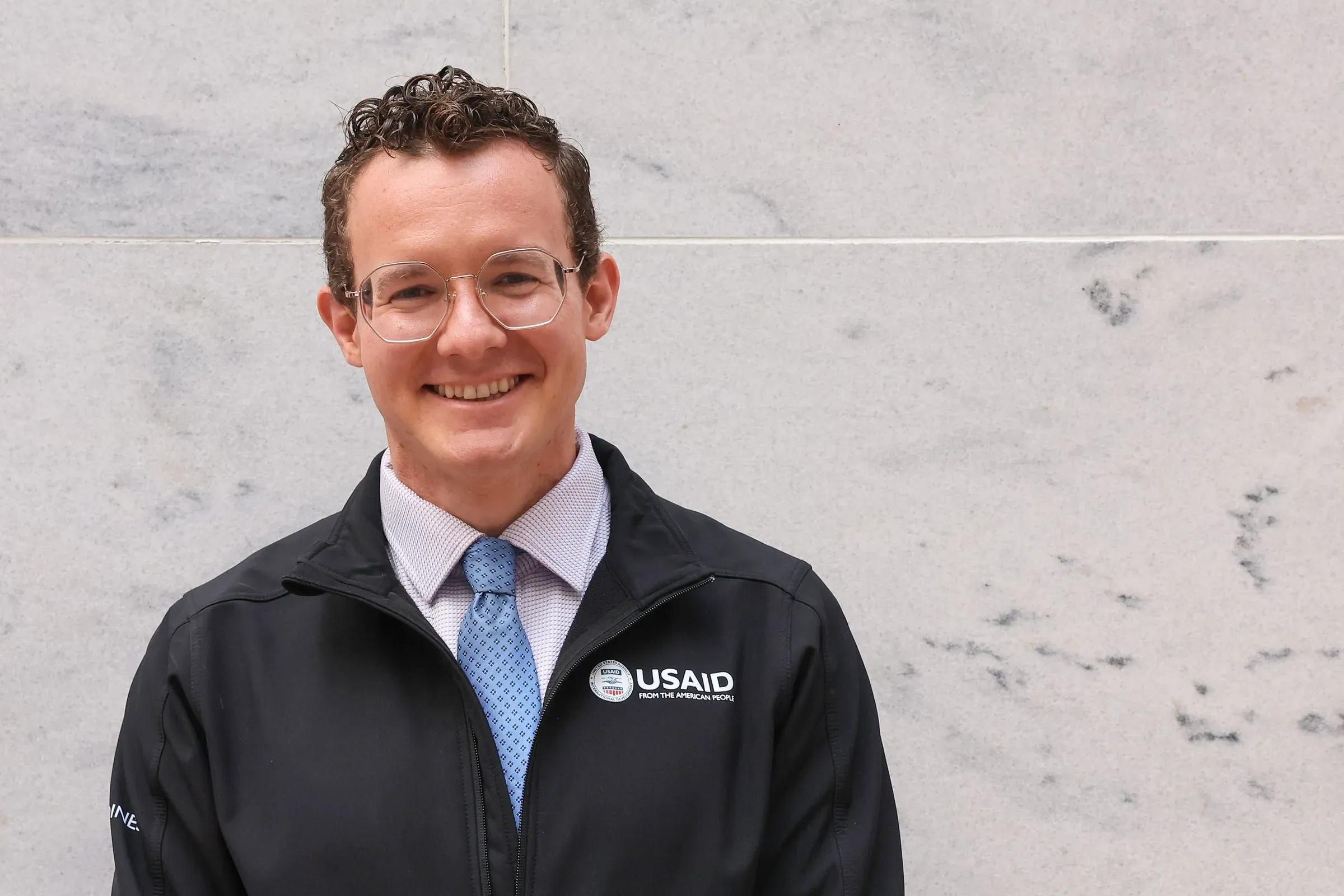 آشلي غارلي، المتعاقدة السابقة في الوكالة الأمريكية للتنمية الدولية، مبتسمة في صورة رسمية، تعكس تحدياتها بعد فقدان وظيفتها.