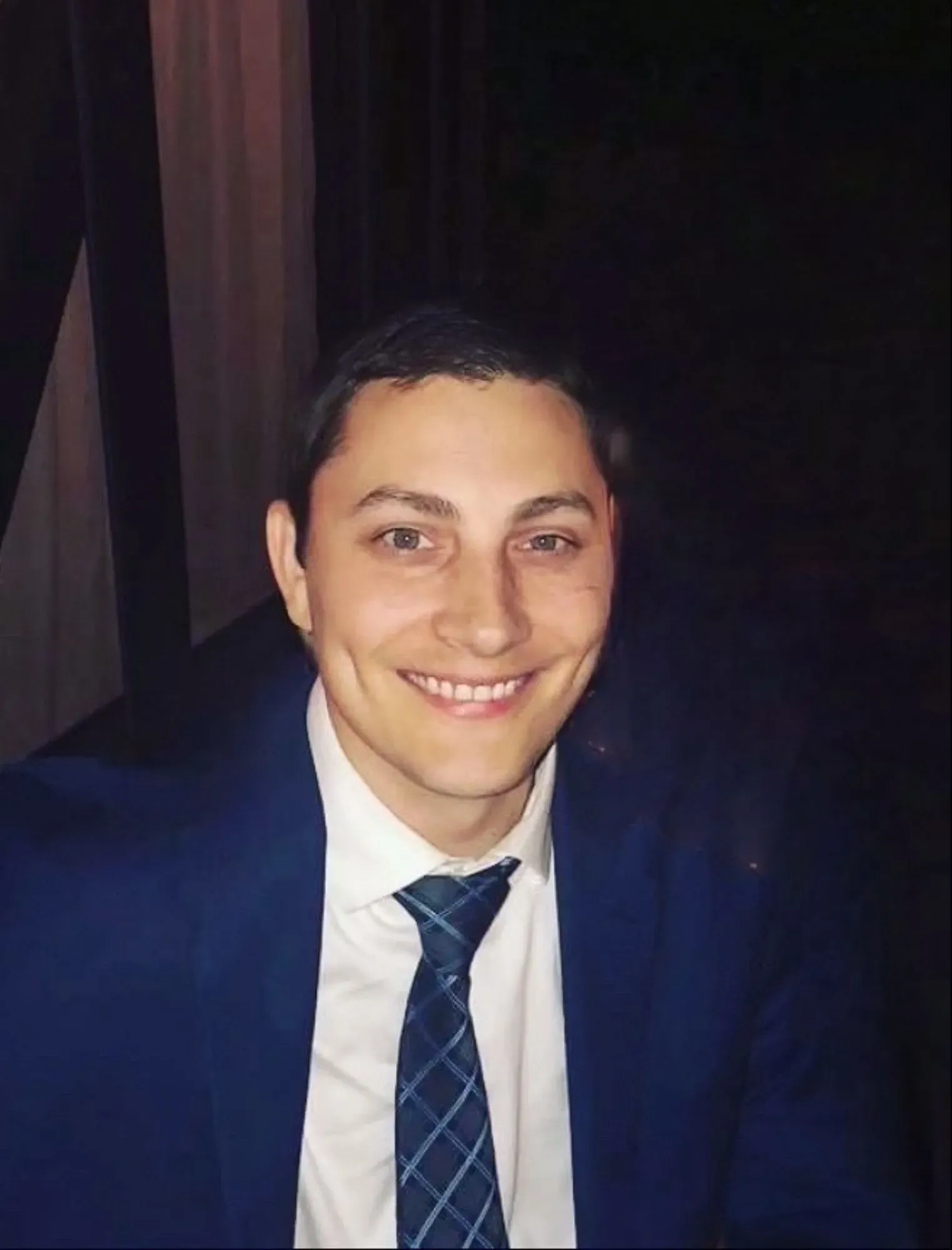 صورة لرجل مبتسم يرتدي بدلة زرقاء وقميص أبيض مع ربطة عنق مزخرفة، تعكس التحديات التي يواجهها العديد من الموظفين الفيدراليين بعد فقدان وظائفهم.