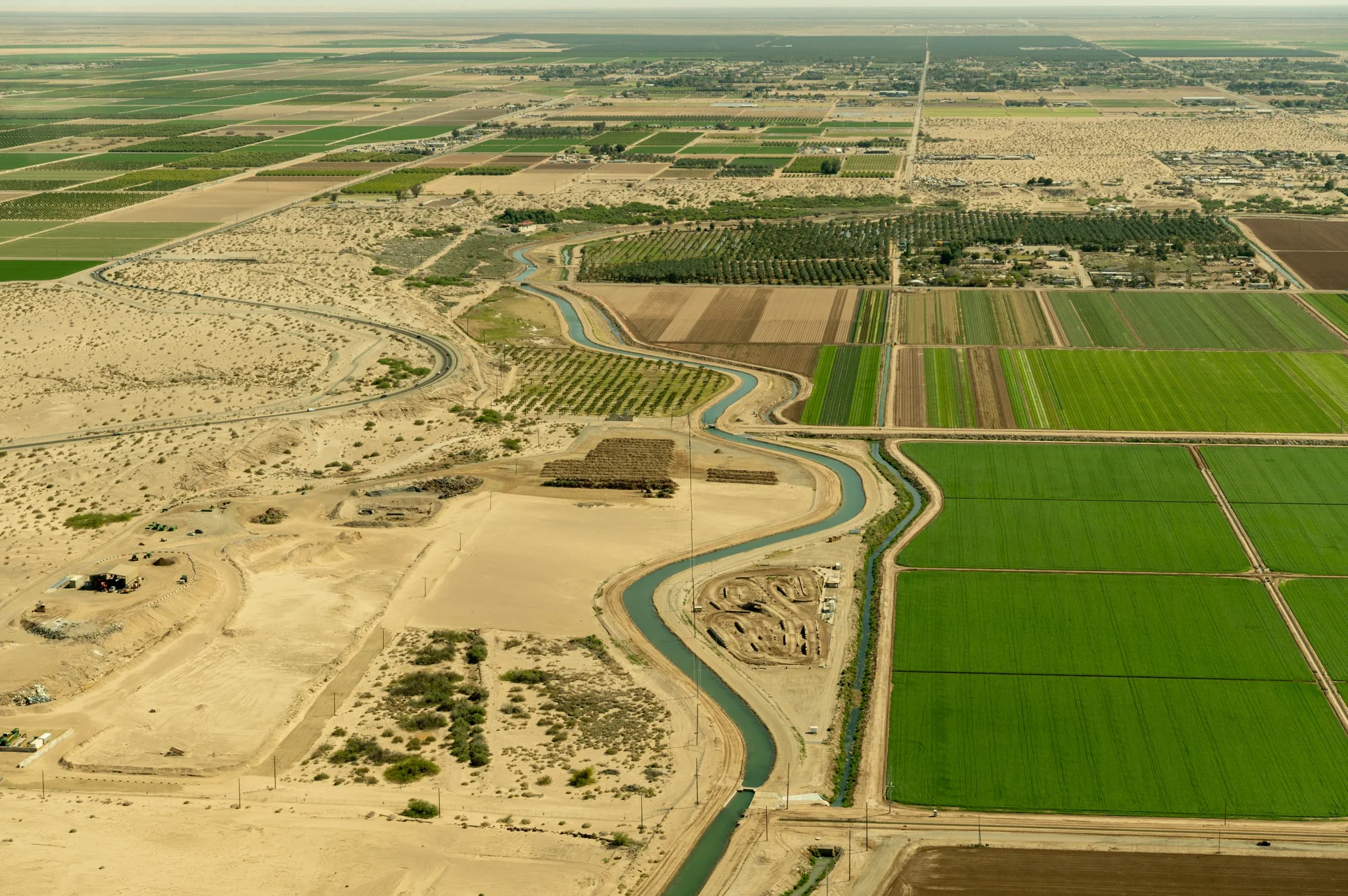 منظر جوي لنهر كولورادو يمر بين أراضٍ زراعية خضراء وصحراوية في الجنوب الغربي الأمريكي، مع تراجع مستويات المياه بسبب الجفاف المستمر.
