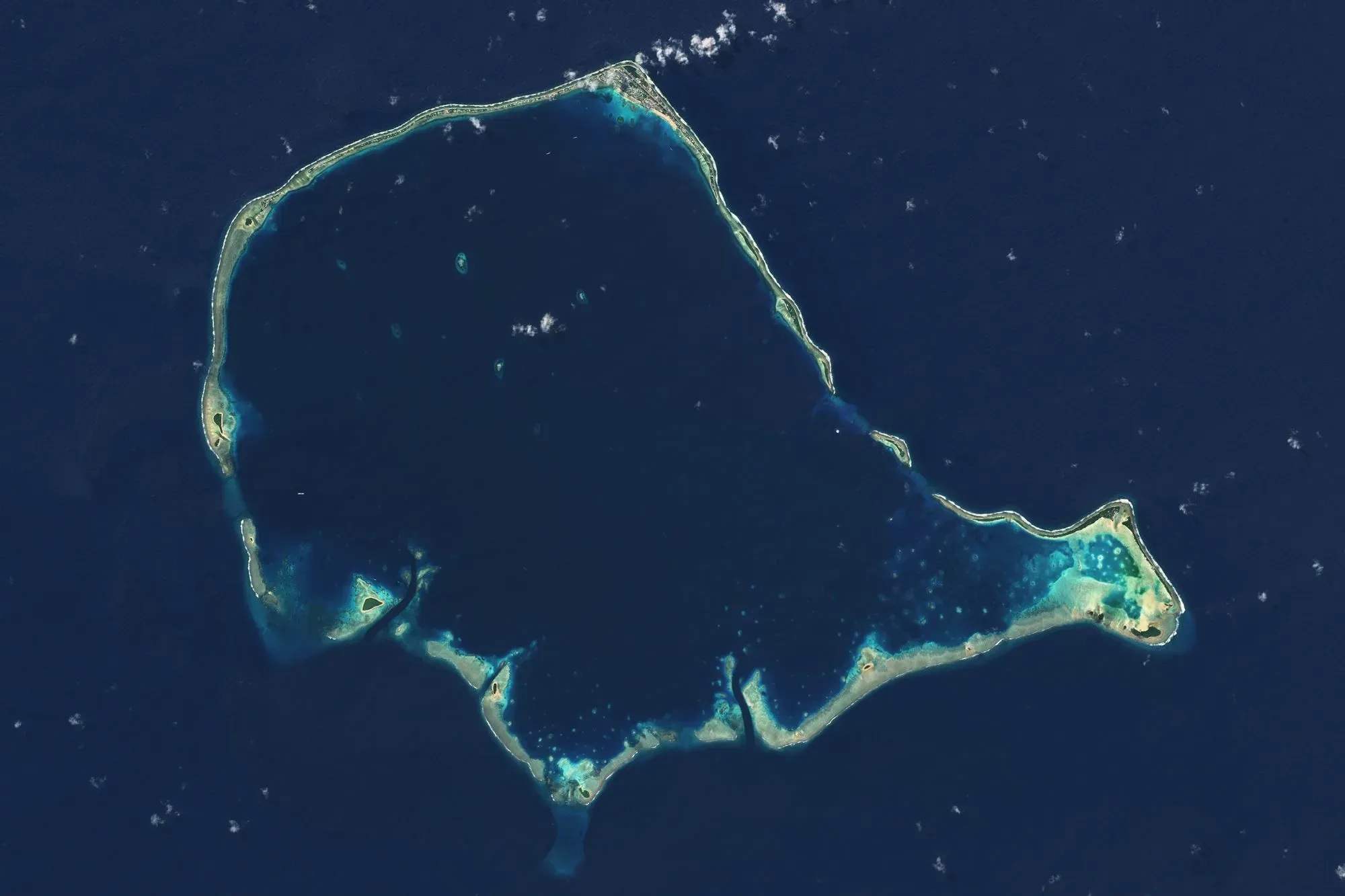 صورة جوية لجزيرة محاطة بمياه زرقاء، تُظهر الشعاب المرجانية والمناطق الساحلية، تعكس تأثيرات تغير المناخ على البيئة البحرية.