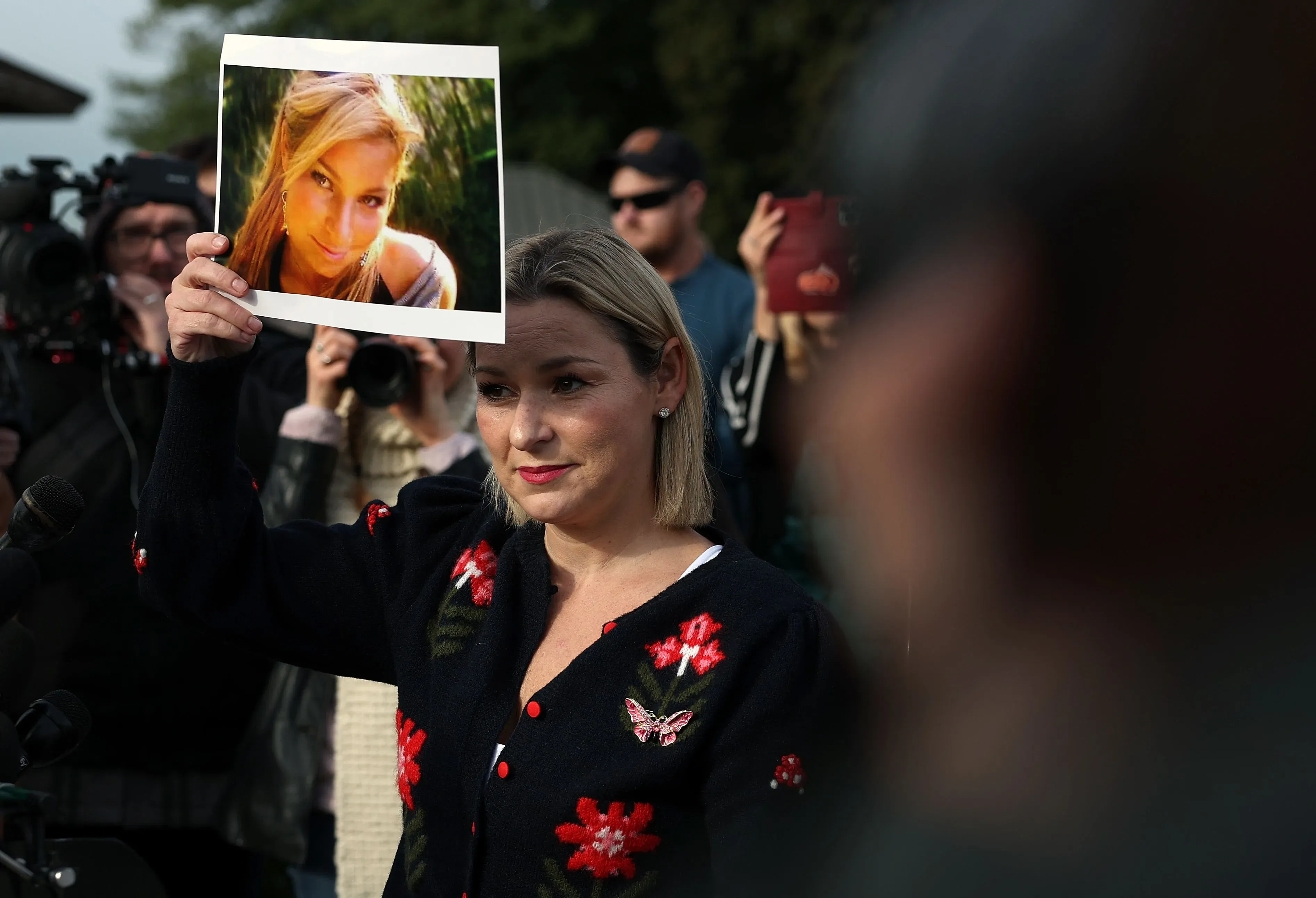 امرأة تحمل صورة لفتاة، وسط حشد من الناس، تعبر عن مشاعر الغضب والقلق بشأن قضايا العدالة المتعلقة بملفات جيفري إبشتاين.