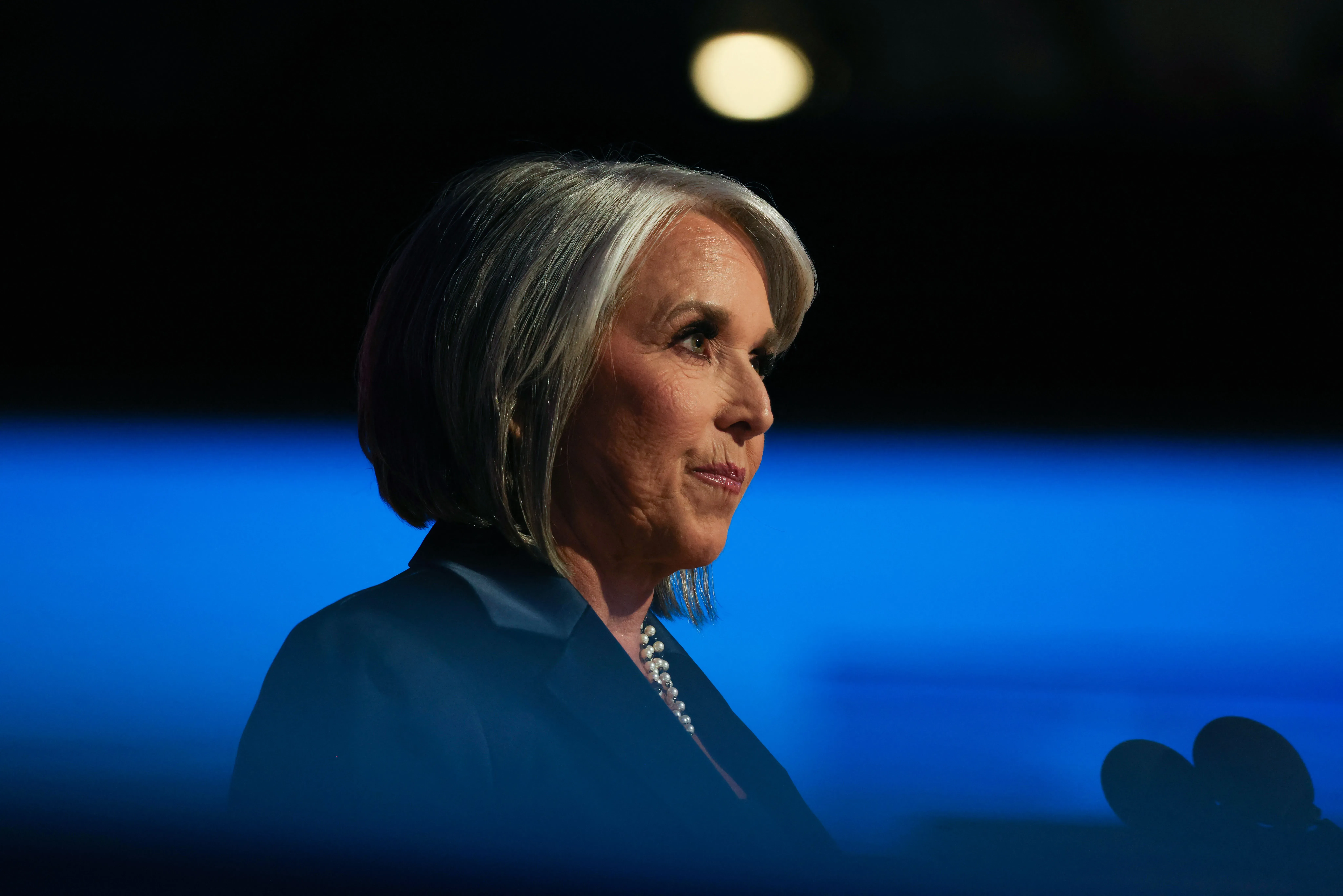 حاكمة نيو مكسيكو ميشيل لوجان غريشام تتحدث في مؤتمر، مع خلفية مضاءة، تعكس جهود الحرس الوطني لمواجهة الجريمة في الولاية.