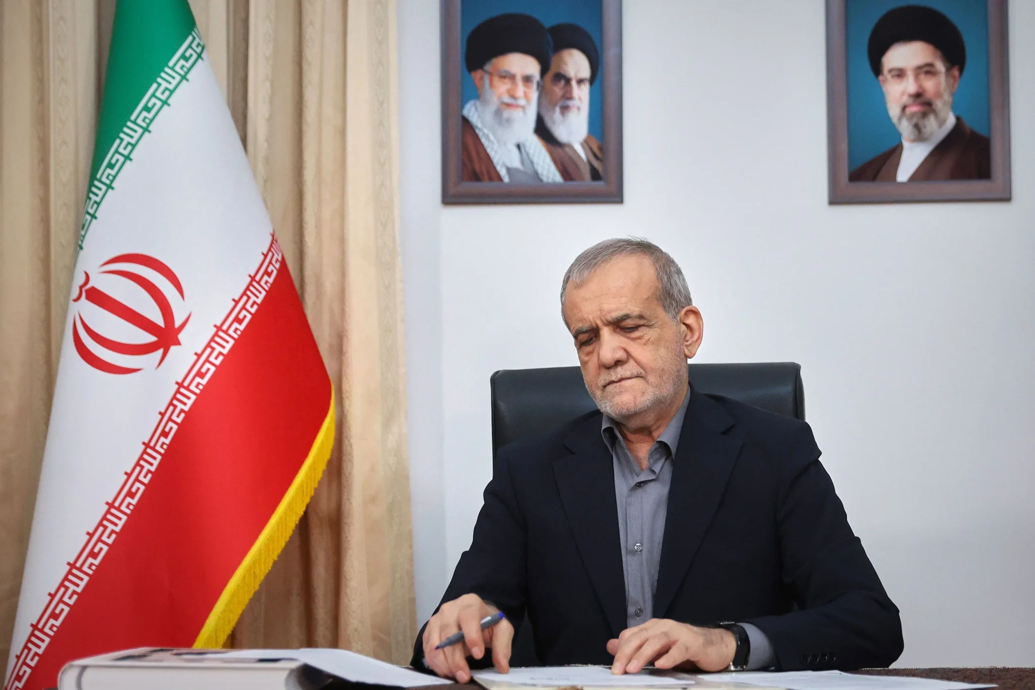 مسؤول إيراني يجلس أمام علم إيران وصور قيادات الجمهورية الإسلامية، في سياق التفاهمات بين طهران وواشنطن لوقف التصعيد في الخليج ومضيق هرمز.