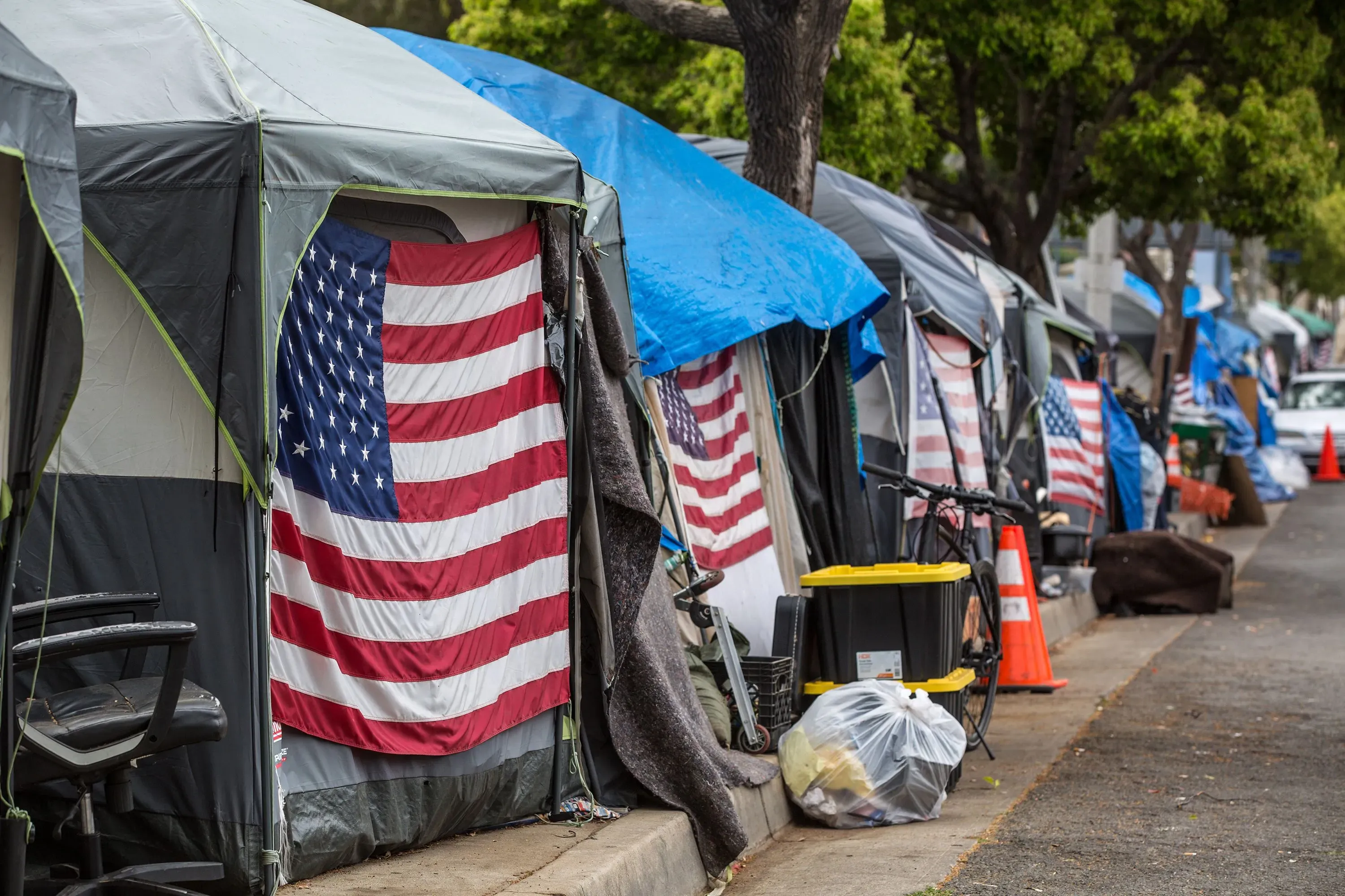 خيام مؤقتة على جانب الطريق مزينة بأعلام أمريكية، تعكس وضع المحاربين القدامى المشردين في ظل القضايا الصحية والقانونية.