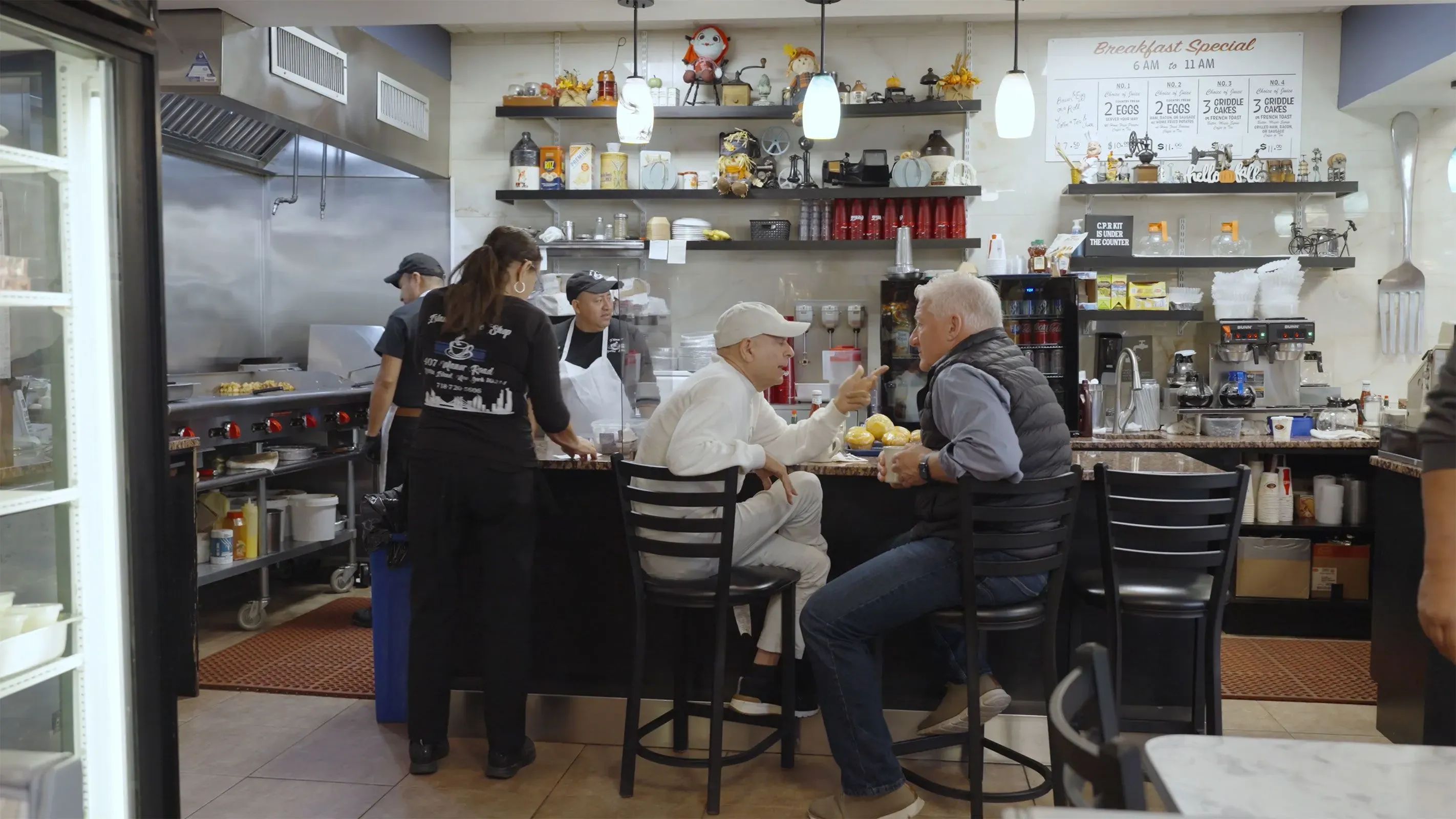 مشهد داخلي لمطعم في بروكلين، حيث يجلس زبائن يتناولون الطعام، مع وجود طاقم العمل في المطبخ خلفهم.