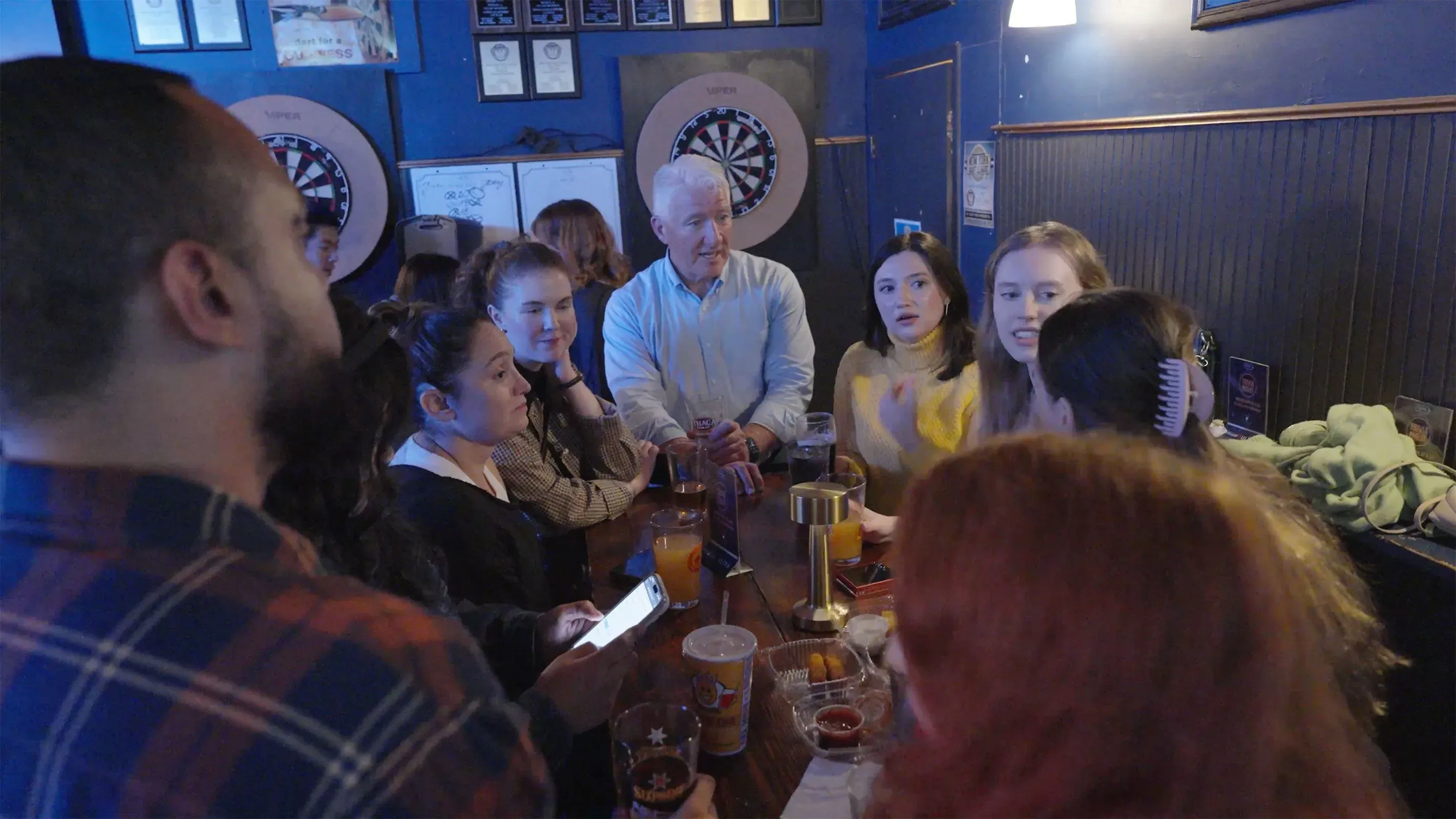 مجموعة من الأشخاص يتحدثون في بار في بروكلين، مع التركيز على تفاعلهم حول الانتخابات المحلية وأهمية التصويت.