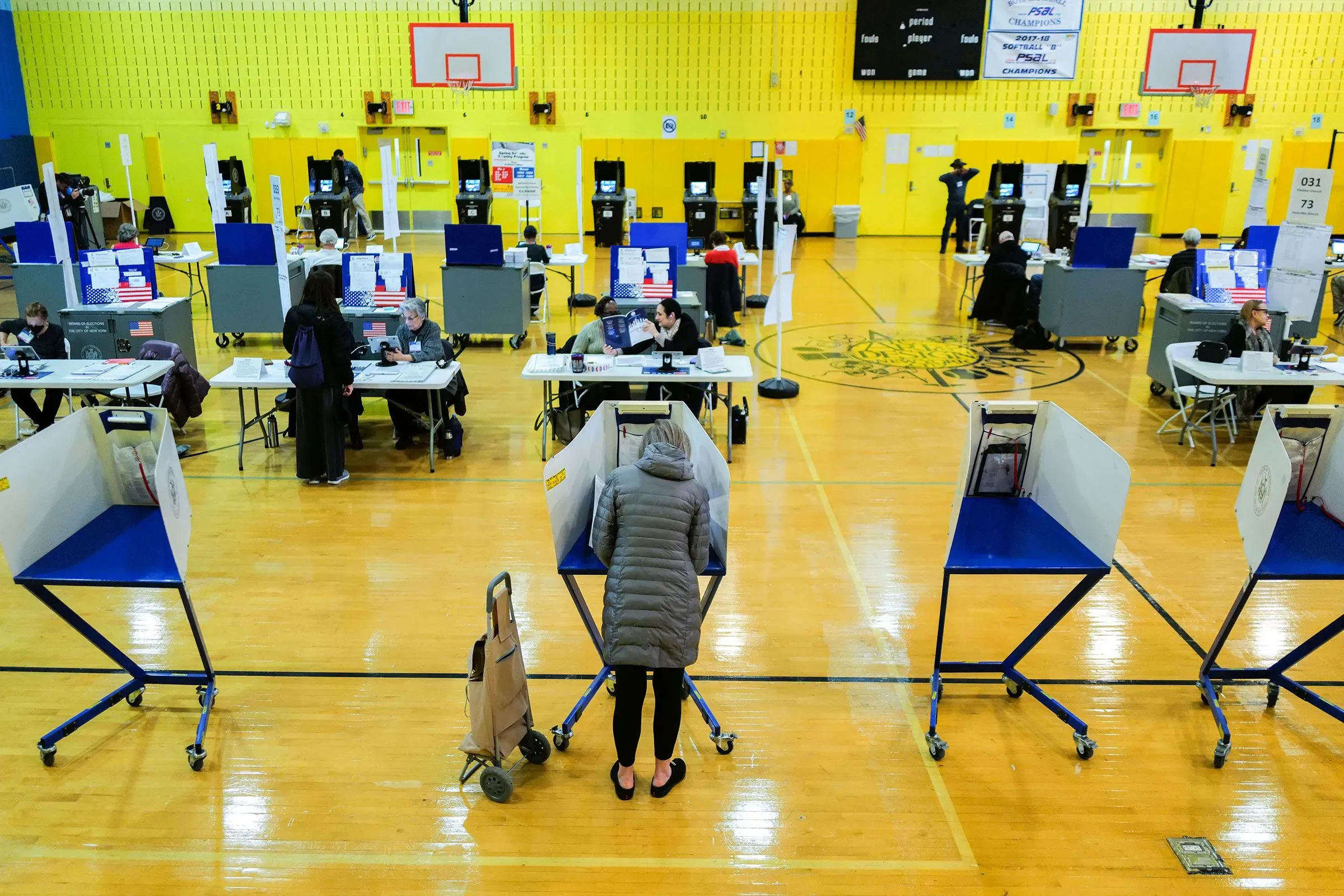 مركز اقتراع في نيويورك حيث يقوم الناخبون بالتصويت، مع وجود آلات الاقتراع وأشخاص يعملون في خلفية الصورة.