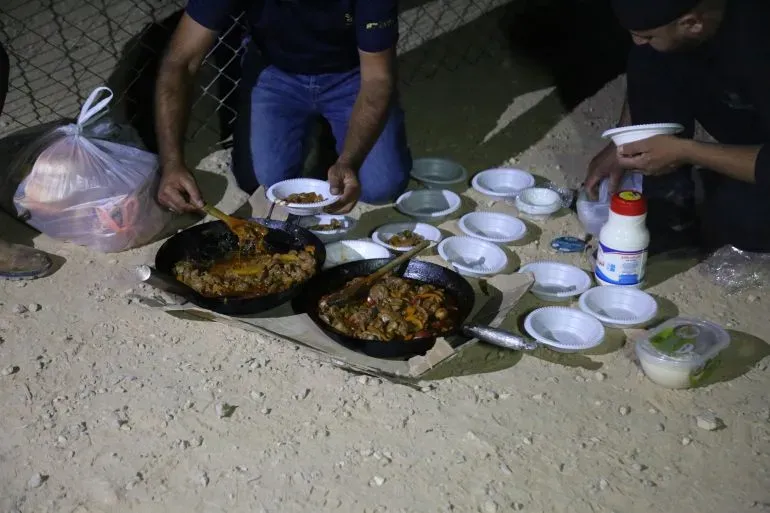 وجبة تقليدية تُقدم في الليل، حيث يجلس رجلان بجانب أطباق الطعام، محاطين بأواني فارغة، في قرية المفقرة.