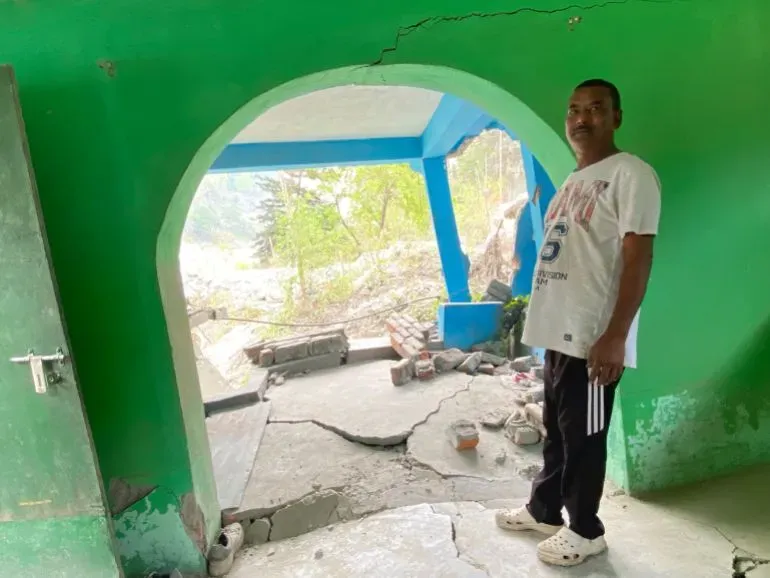 رجل يقف داخل منزل متصدع في قرية ناغا، سيكيم، بعد الفيضان المدمر الناتج عن انهيار بحيرة جليدية، مع آثار الدمار واضحة حوله.