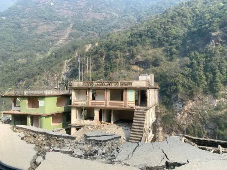 مبنى متصدع في قرية ناغا بولاية سيكيم، يظهر آثار الفيضانات والانهيارات الأرضية، مع تلال خضراء في الخلفية.