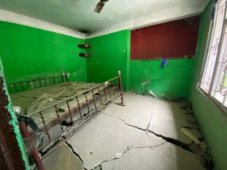 غرفة متضررة في قرية ناغا بسكيكيم، تظهر شقوقًا عميقة في الأرضية وجدرانًا متصدعة، تعكس آثار الفيضانات والانهيارات الأرضية.