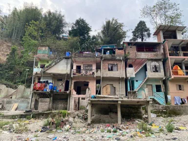 منازل متصدعة ومهجورة في قرية ناغا بولاية سيكيم، تعكس آثار الفيضان المدمر الناتج عن انهيار بحيرة جليدية، مع بقايا الحطام في الأسفل.