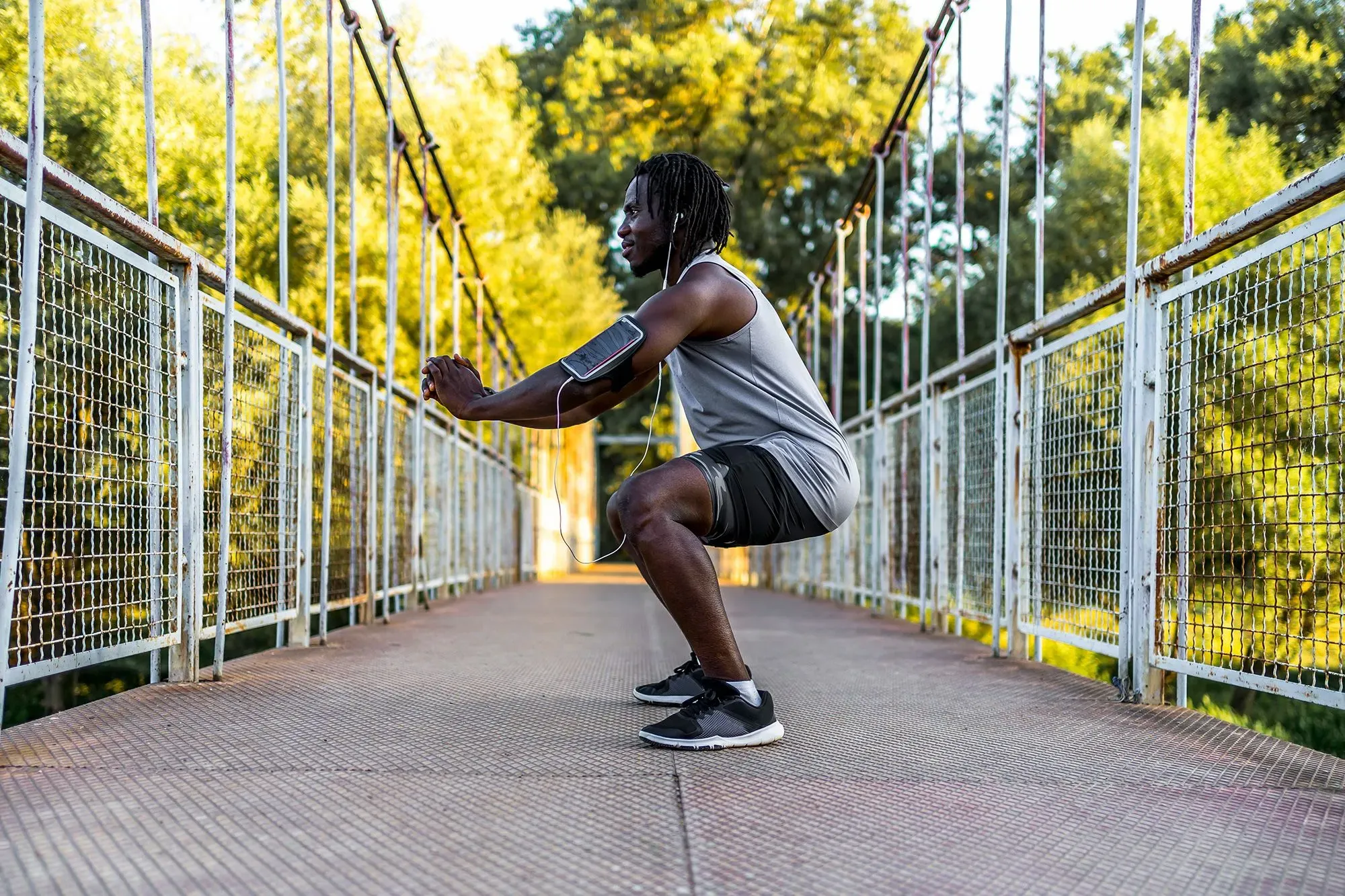 رجل يقوم بتمرين القرفصاء على جسر، مع التركيز على تقنيات وزن الجسم لبناء القوة وتحسين اللياقة البدنية.