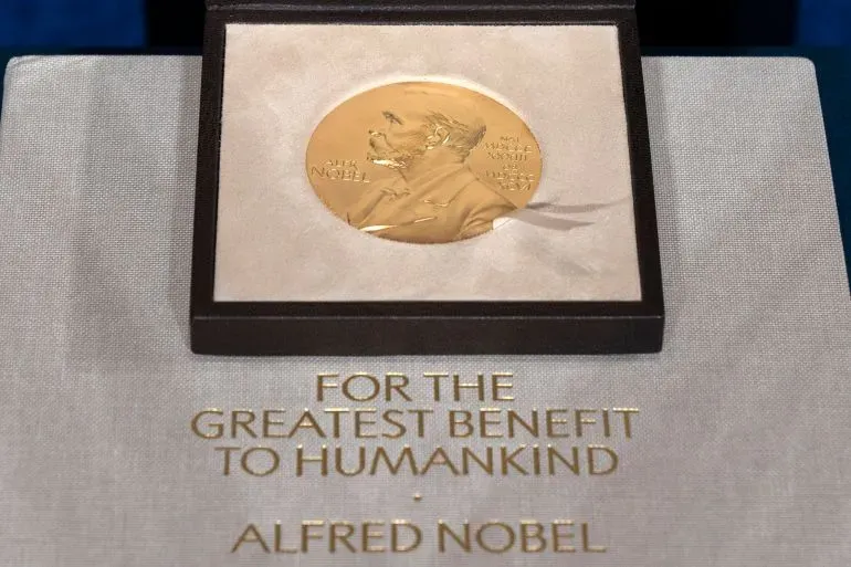 ميدالية جائزة نوبل الذهبية موضوعة داخل علبة، مع نقش "لأكبر فائدة للبشرية" تحت صورة ألفريد نوبل، تشير إلى إنجازات الفائزين في العلوم.