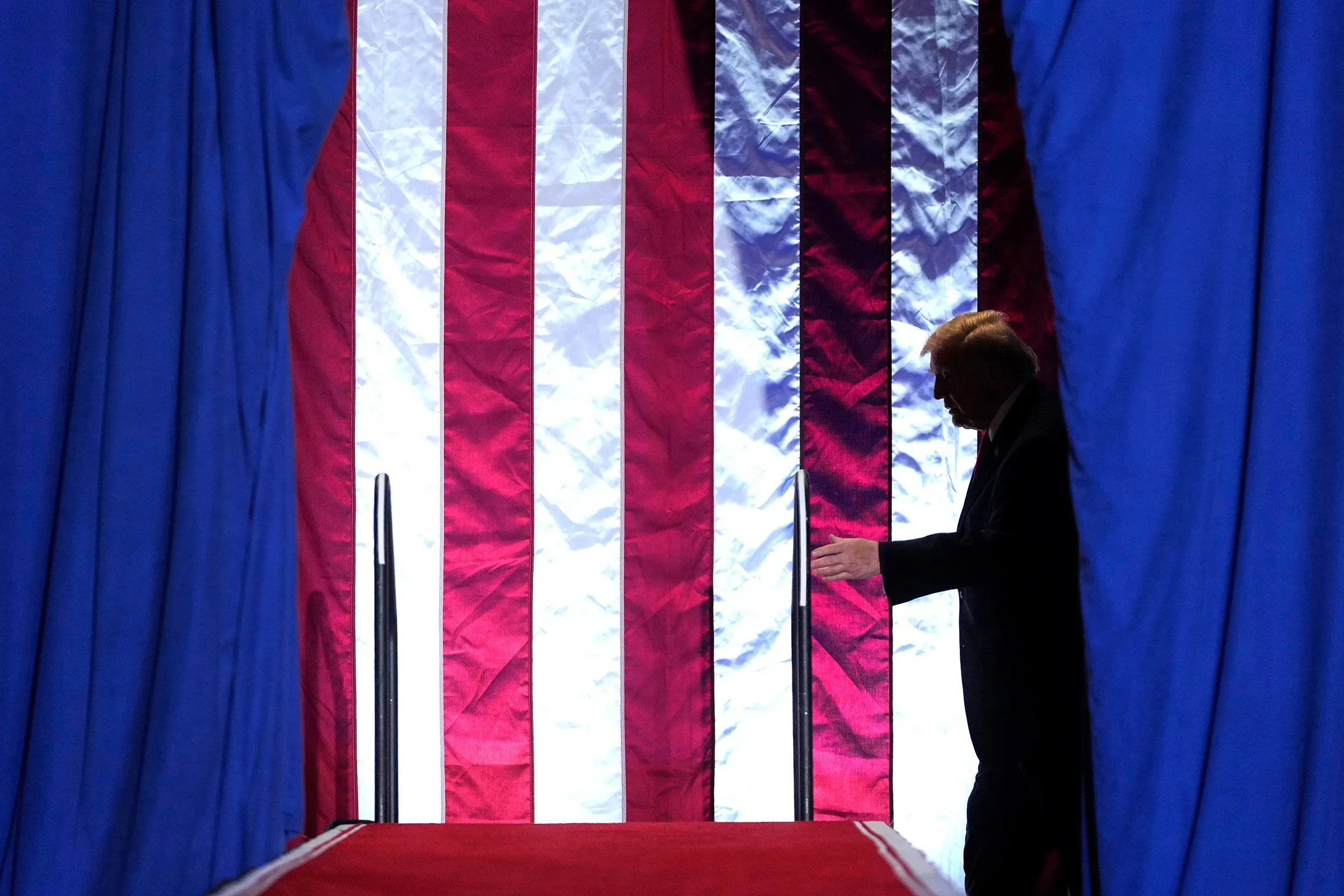 ظل الرئيس ترامب يسير نحو منصة حمراء، محاطًا بألوان العلم الأمريكي، في سياق حديثه عن قضايا الهجرة والأمن.