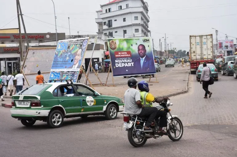 ملصقات انتخابية للمرشحين الرئاسيين في برازافيل، مع حركة المرور والمارة في السوق، تعكس أجواء الانتخابات المقبلة.