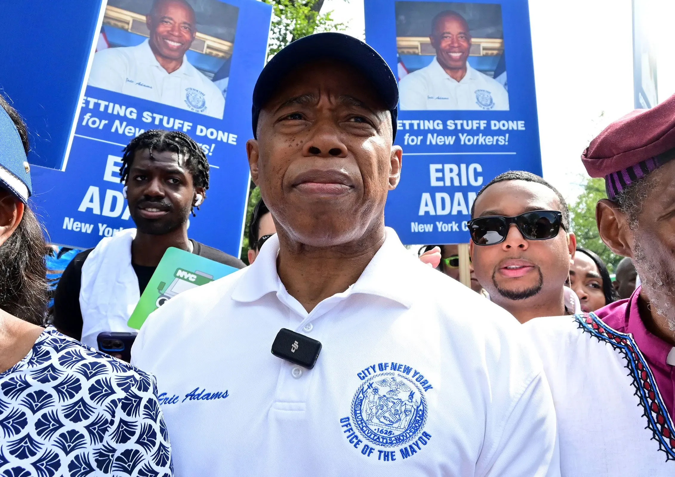 إريك آدامز، عمدة نيويورك، يشارك في تجمع جماهيري، محاطًا بداعمين، مع لافتات تدعمه في حملته الانتخابية.