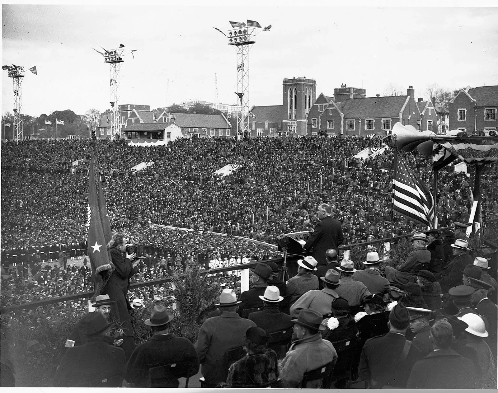 تجمع حاشد في حدث تاريخي، حيث يتحدث أحد القادة أمام جمهور كبير، مع أعلام ترفرف في الخلفية.