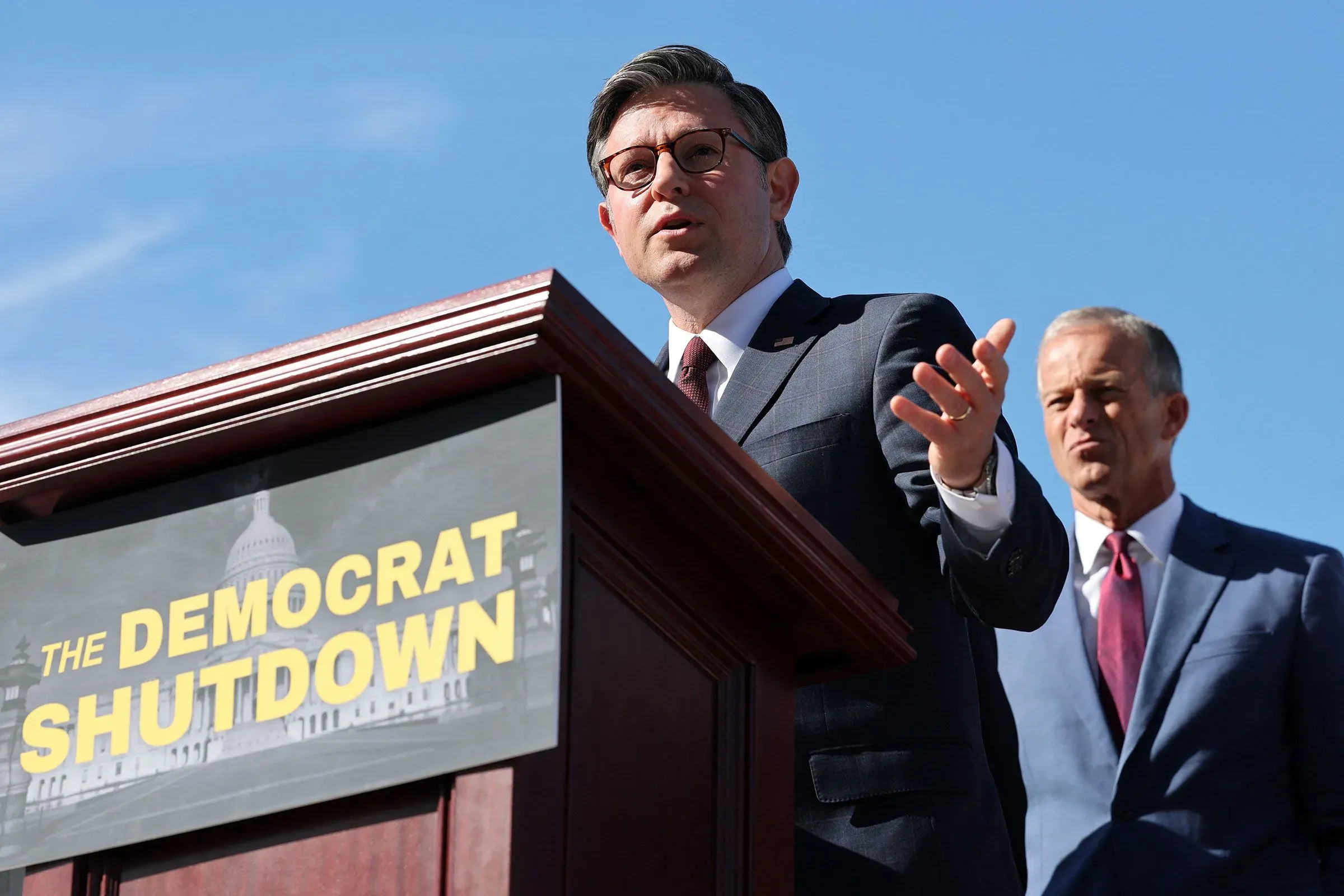 رجل يتحدث من منصة أمام لافتة تحمل عبارة "الإغلاق الديمقراطي"، في سياق مناقشات حول قضايا الرعاية الصحية والسياسة الأمريكية.