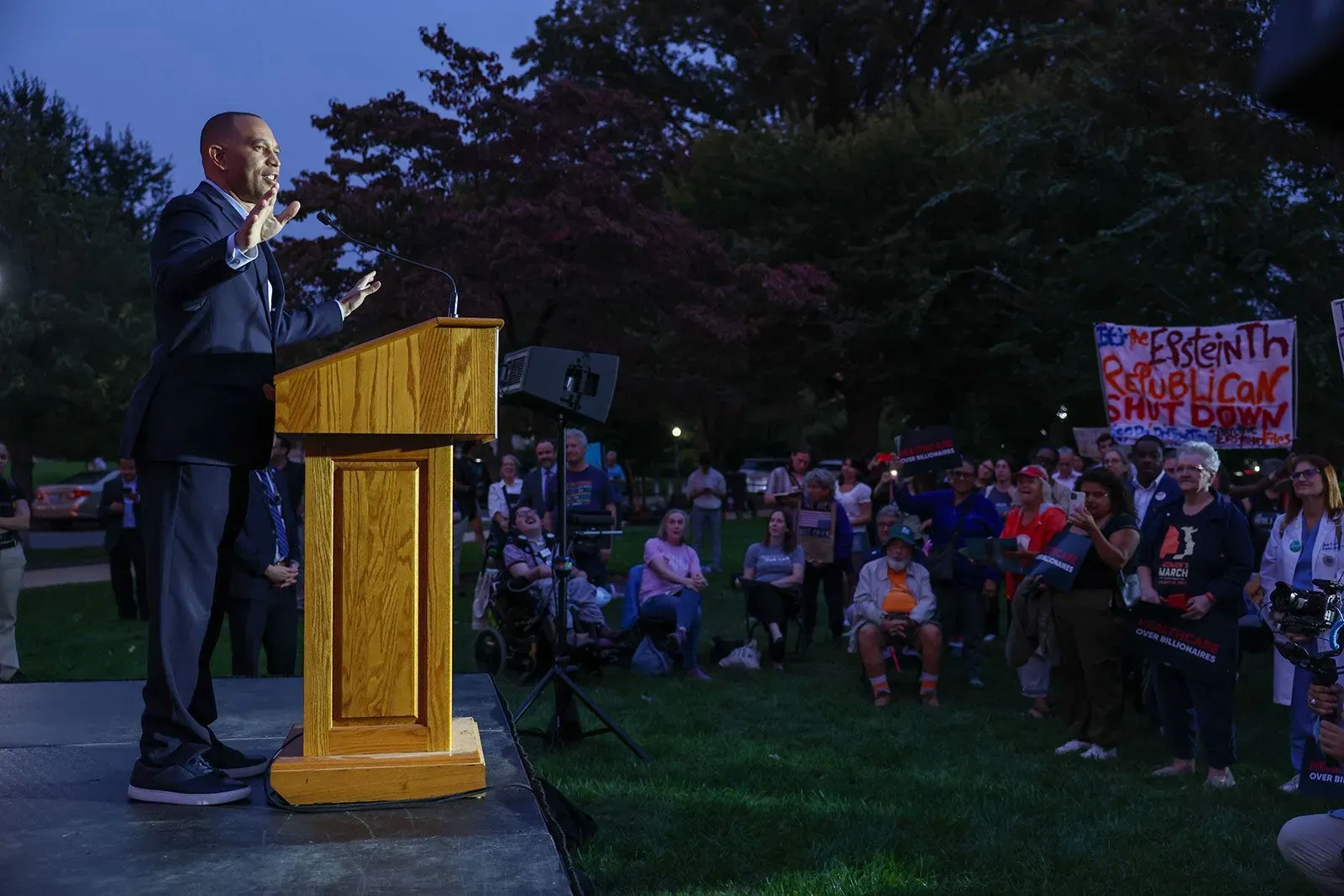 مظاهرة في واشنطن حيث يتحدث متحدث أمام حشد من الناس، مع لافتات تدعو لدعم الرعاية الصحية، في أجواء سياسية مشحونة.