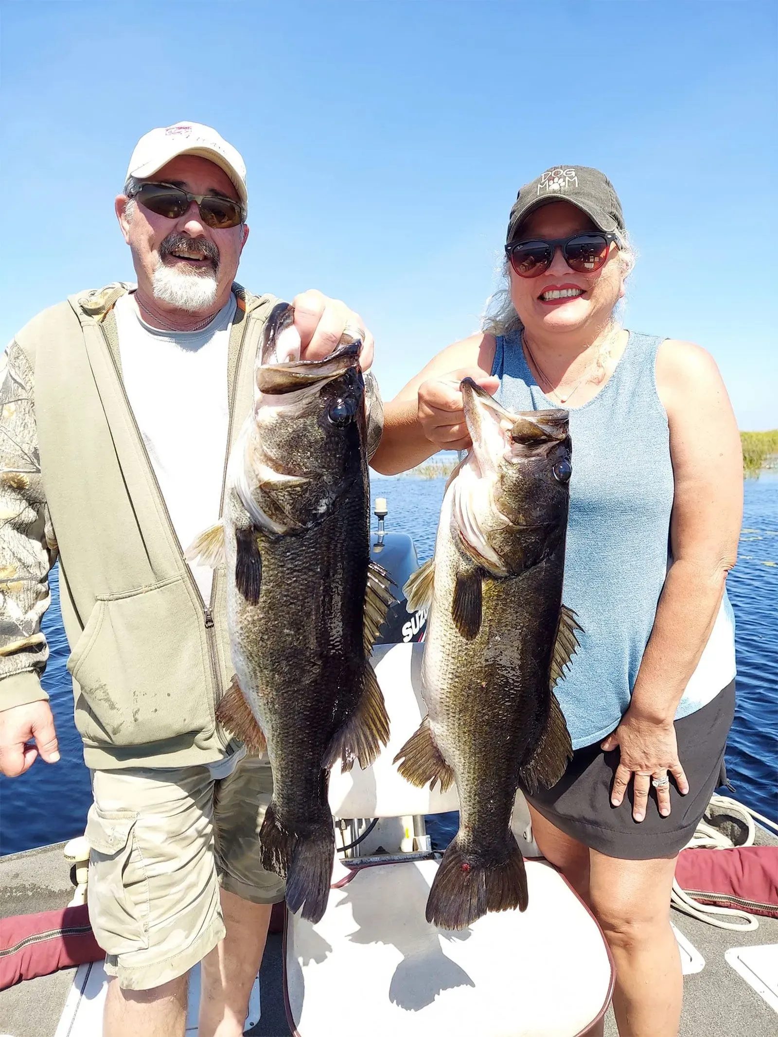 امرأة ورجل يحملان سمكتين كبيرتين في قارب، يظهران الابتسامة في يوم مشمس. الصورة تعكس اللحظات السعيدة في الأنشطة الخارجية.