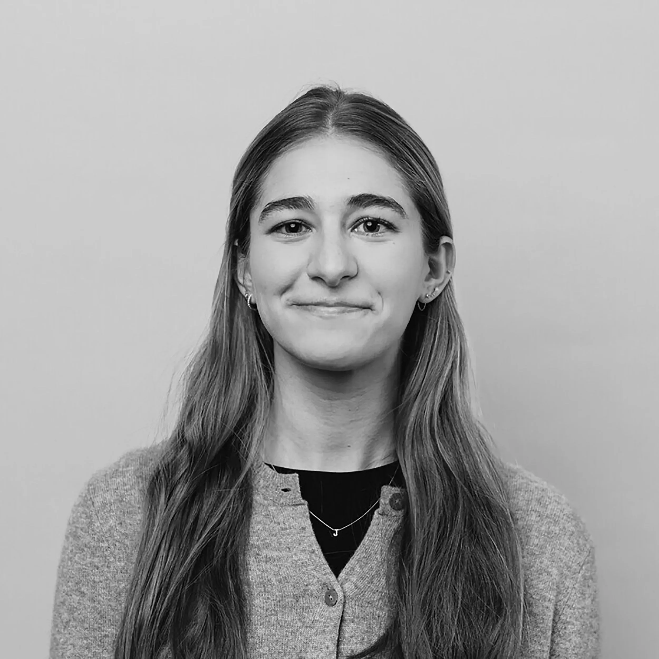 صورة شابة مبتسمة ذات شعر طويل، ترتدي سترة رمادية، تعكس شعور الأمان والتواصل مع زملائها في العمل.