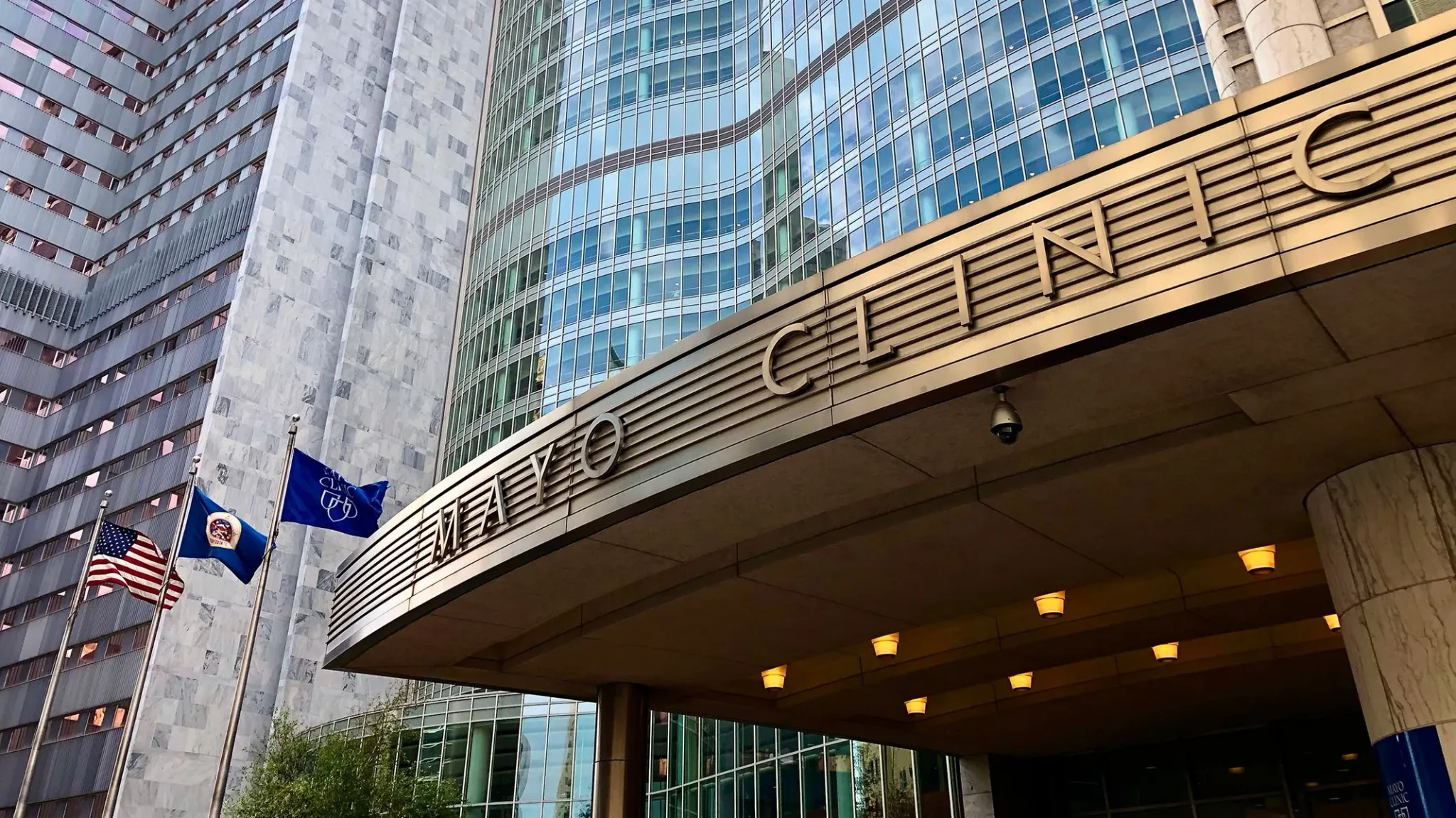 واجهة مبنى Mayo Clinic في مدينة كبيرة مع أعلام الولايات المتحدة وعلم المستشفى، تعكس دور المؤسسة الرائد في الطب والذكاء الاصطناعي.