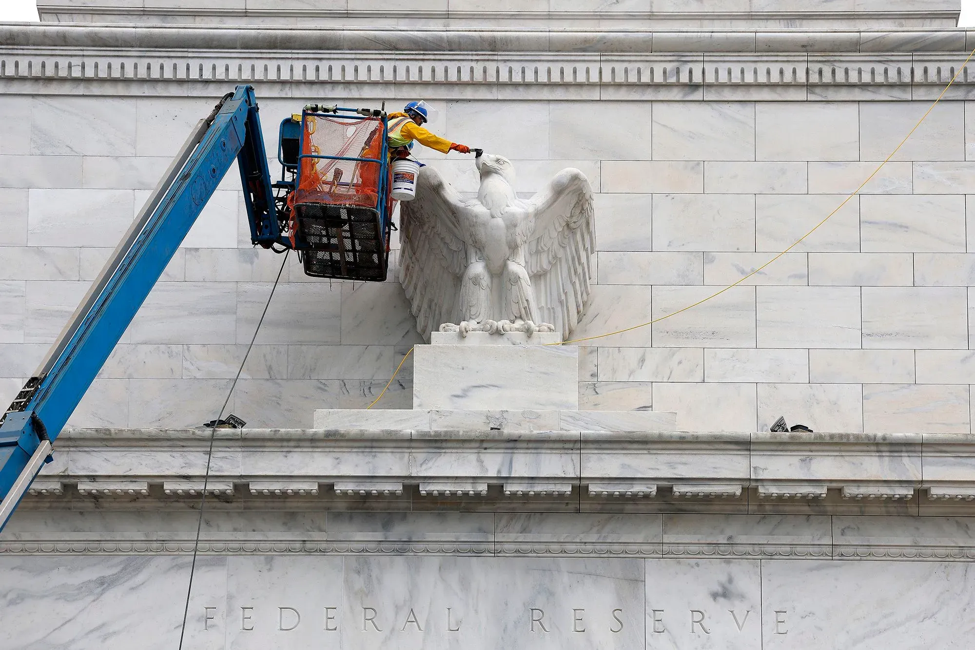 عامل يقوم بأعمال صيانة على واجهة مبنى الاحتياطي الفيدرالي، حيث يظهر النسر الرمزي، مما يعكس أهمية البنك المركزي في الاقتصاد الأمريكي.