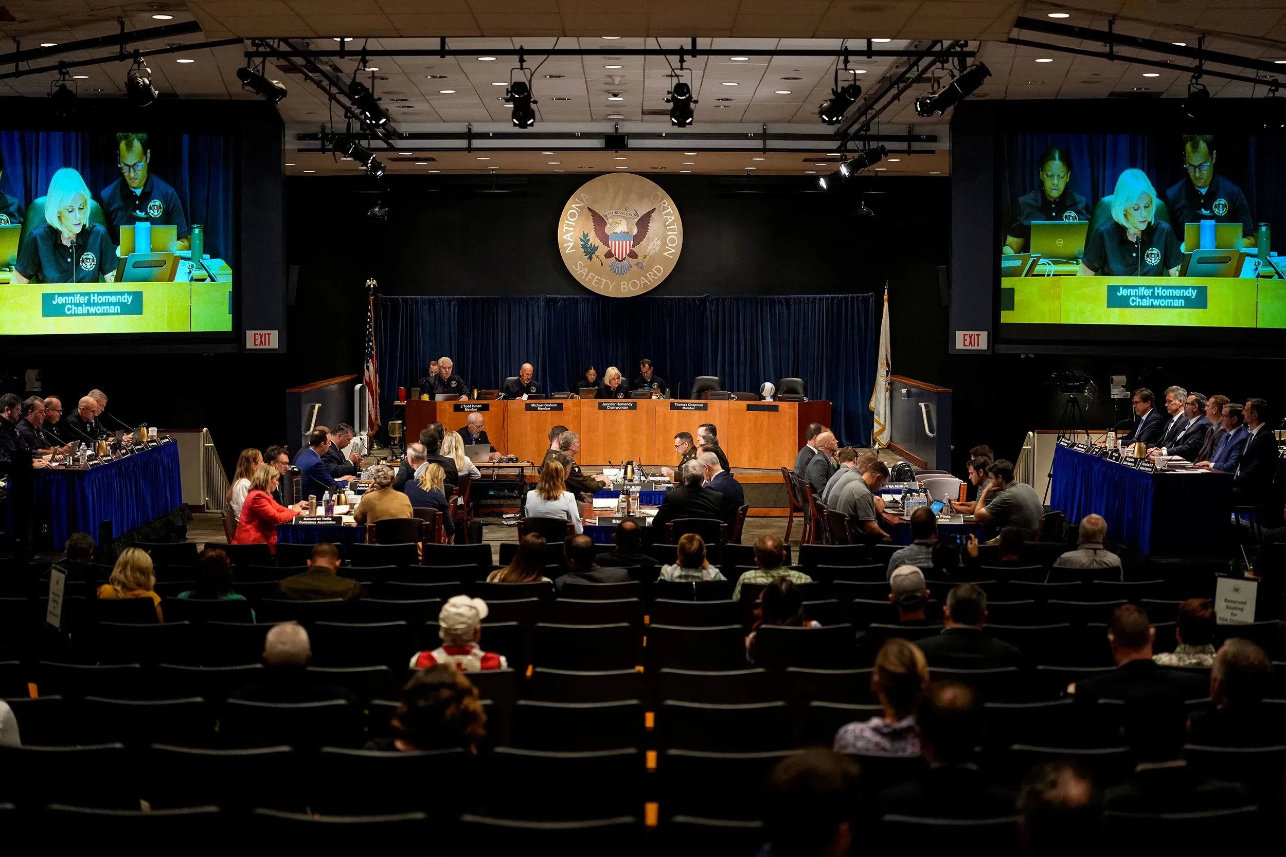 اجتماع المجلس الوطني لسلامة النقل لمناقشة حادث التصادم الجوي، مع وجود أعضاء المجلس وخلفية تتضمن شاشات عرض.