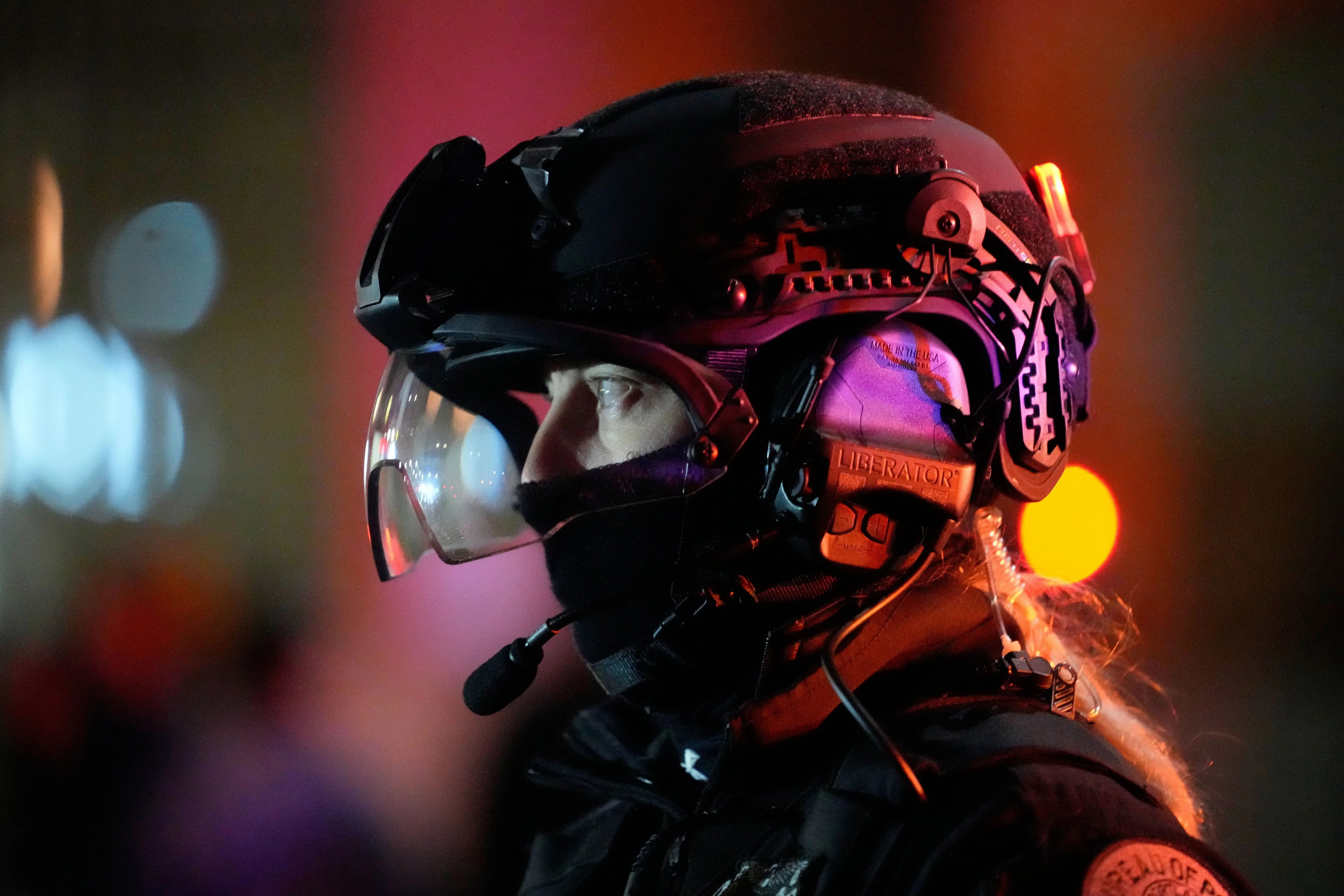 شرطي يرتدي خوذة ومعدات خاصة، يظهر في موقع حادث إطلاق نار في بورتلاند، وسط أضواء ملونة، مع تصاعد التوترات حول تدخل الفيدراليين.