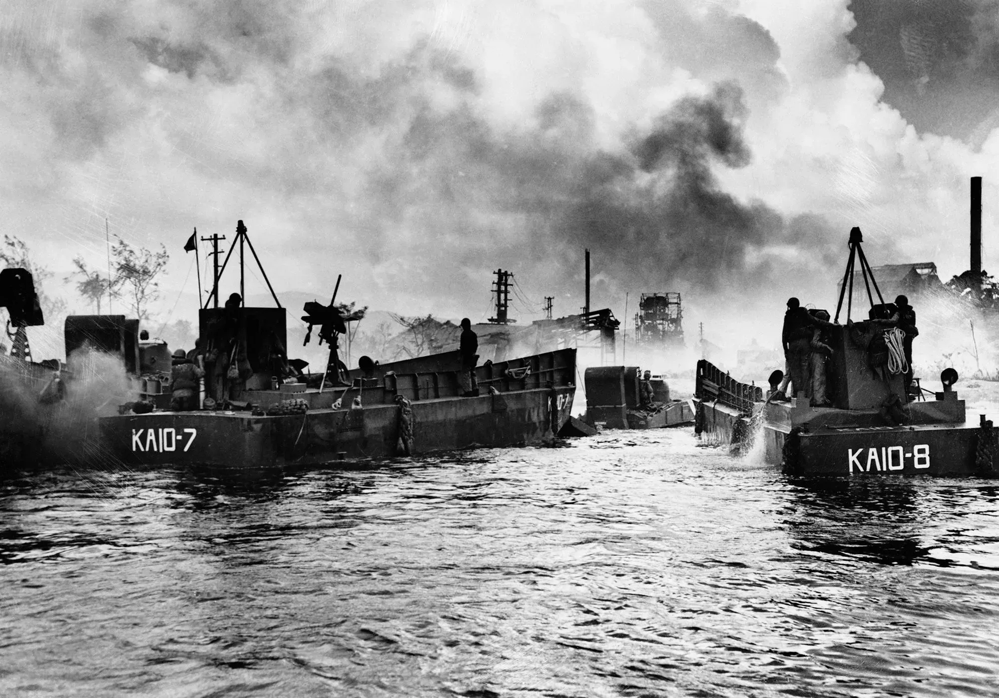 قوارب حربية تبحر في مياه ميناء سايبان، محاطة بدخان المعركة، مع وجود علامات على حطام الحرب العالمية الثانية.