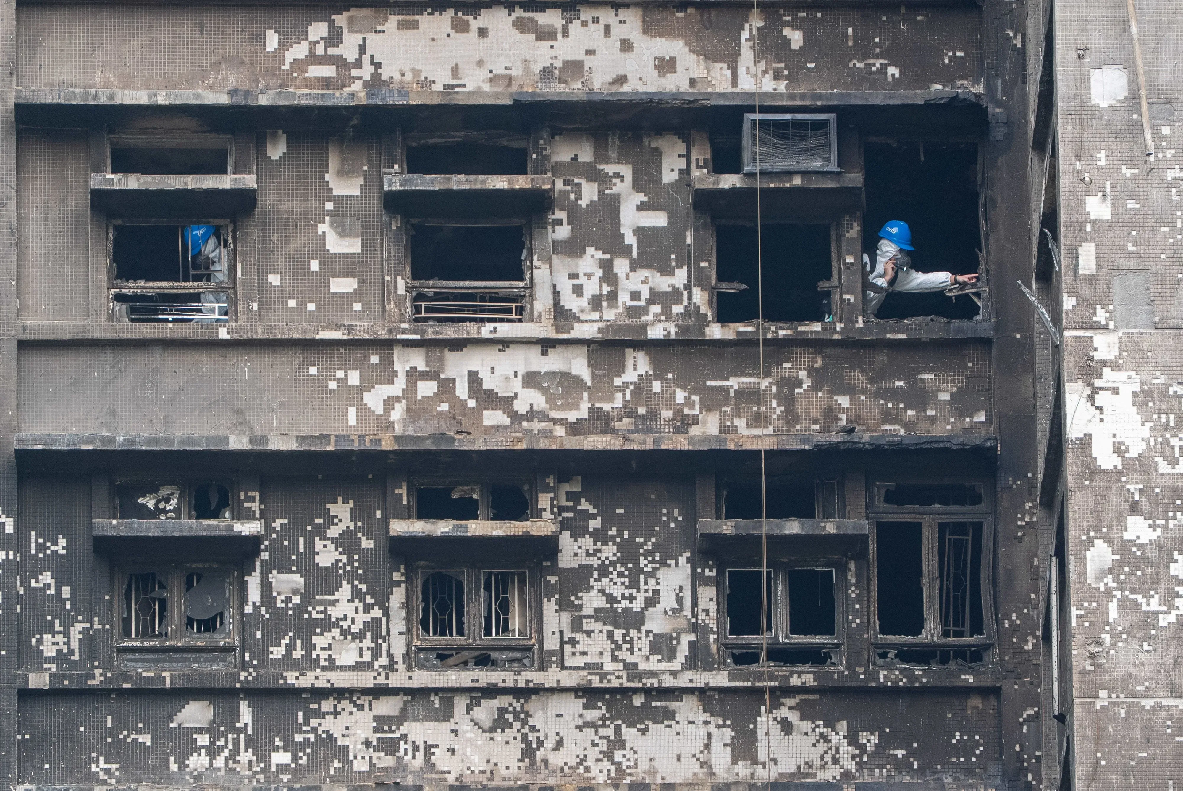 عمال يرتدون خوذات يقومون بتفتيش مبنى محترق في هونغ كونغ، حيث تضررت النوافذ والجدران، في إطار جهود تحديد هوية الضحايا.