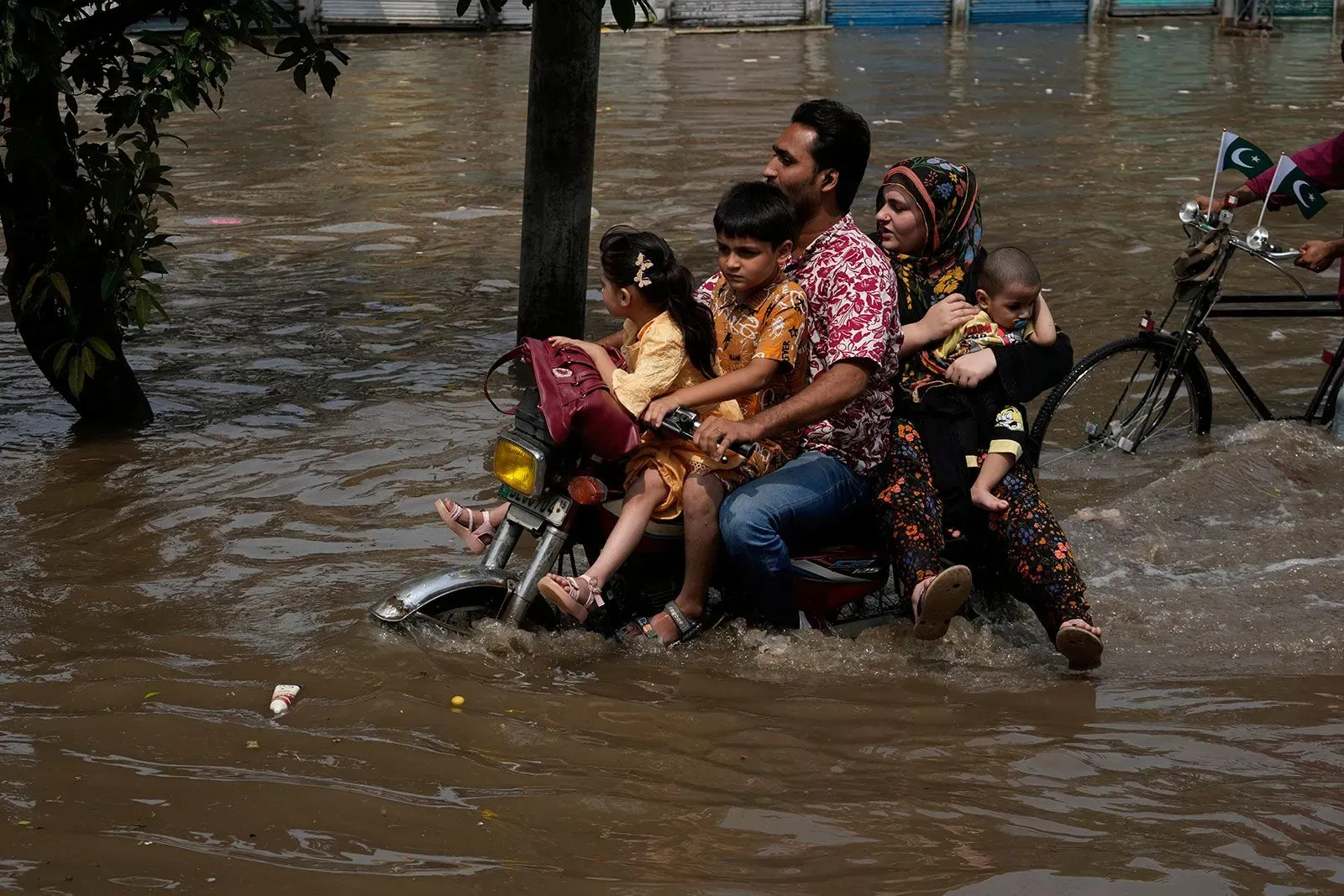 عائلة تتنقل على دراجة نارية وسط مياه الفيضانات في باكستان، تعكس تأثير الأمطار الغزيرة الناتجة عن تغير المناخ على المجتمعات المحلية.