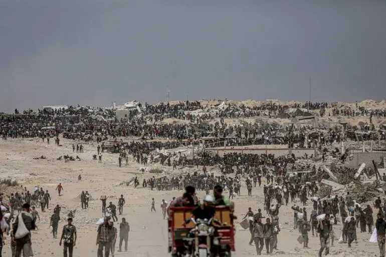 تجمع حشود من الفلسطينيين في منطقة دير البلح بغزة، بحثًا عن المساعدات الإنسانية وسط الدمار الناتج عن القصف الإسرائيلي.