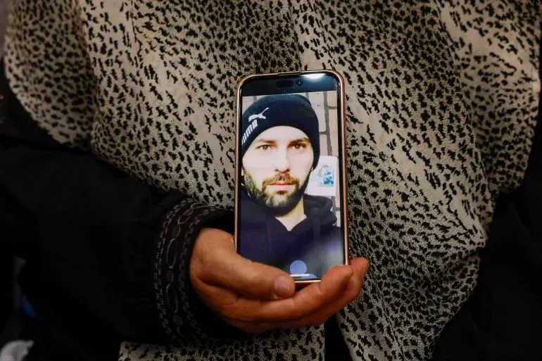 رجل يحمل هاتفًا محمولًا يظهر صورة شاب فلسطيني، في سياق الأحداث العنيفة التي شهدتها بلدة سلواد بالضفة الغربية.