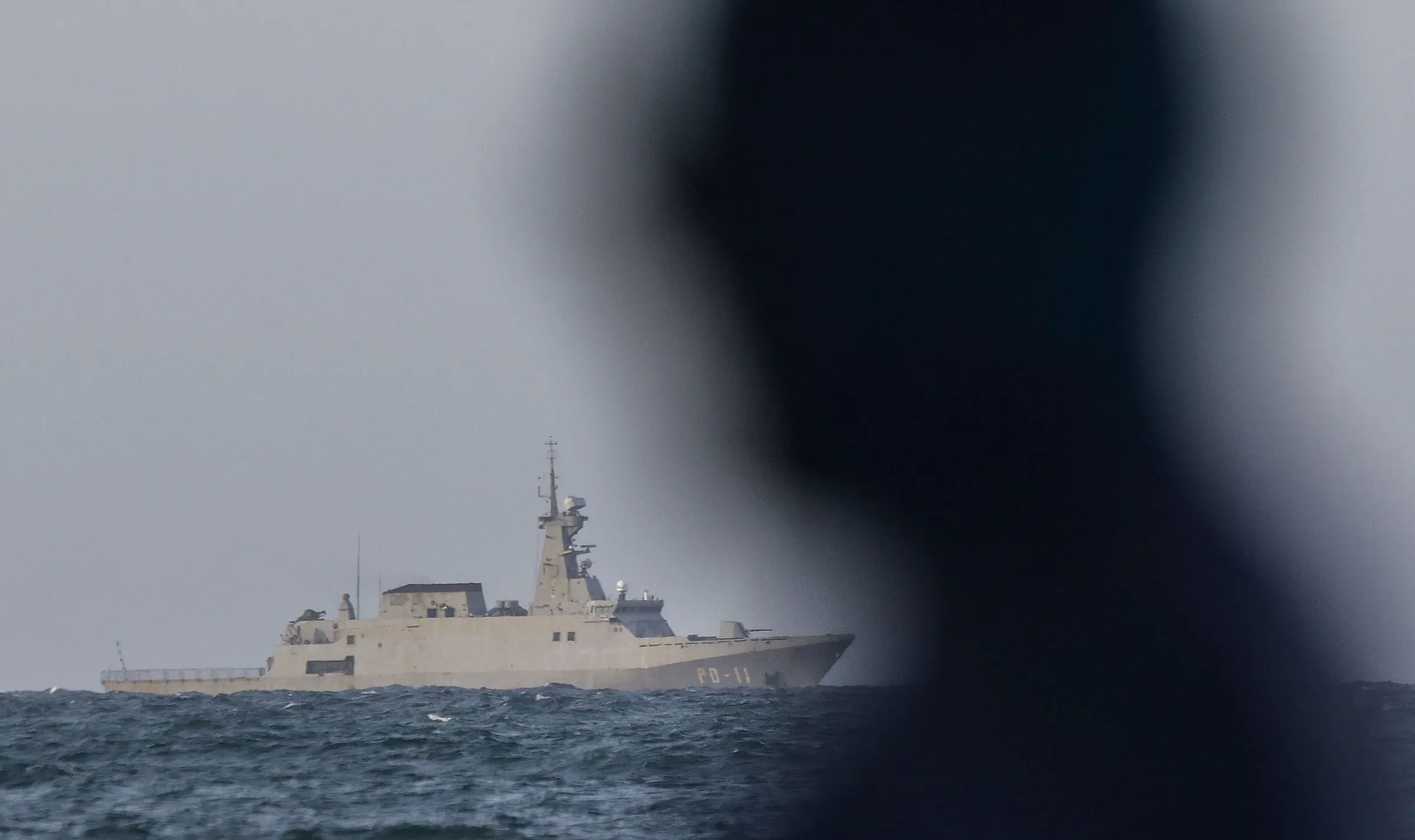 سفينة بحرية تظهر في الخلفية مع ظل شخص في المقدمة، تعكس التوترات السياسية والعسكرية المرتبطة بحملة ترامب الانتقامية.