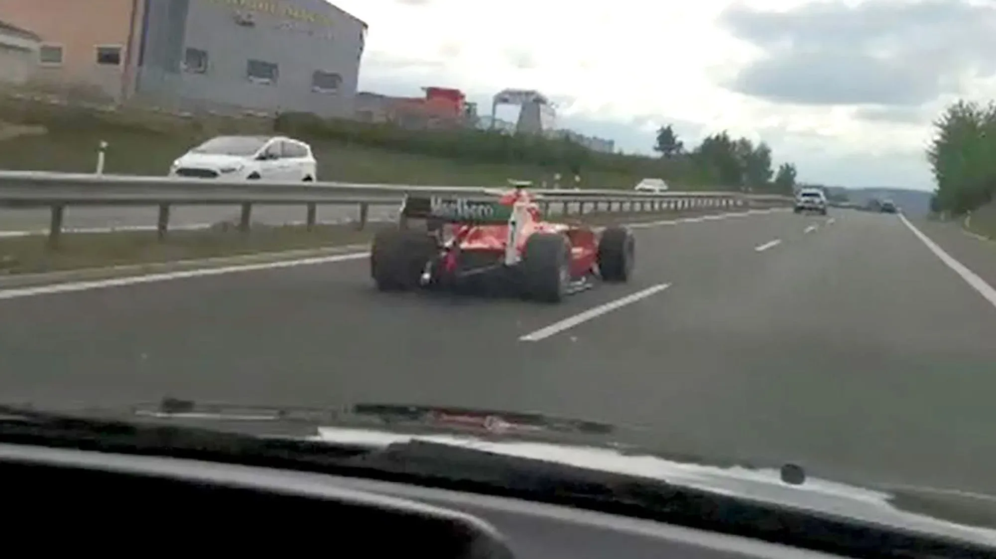 سيارة سباق حمراء تشبه سيارات الفورمولا واحد تسير بسرعة على الطريق السريع، مع وجود سيارات أخرى في الخلفية.